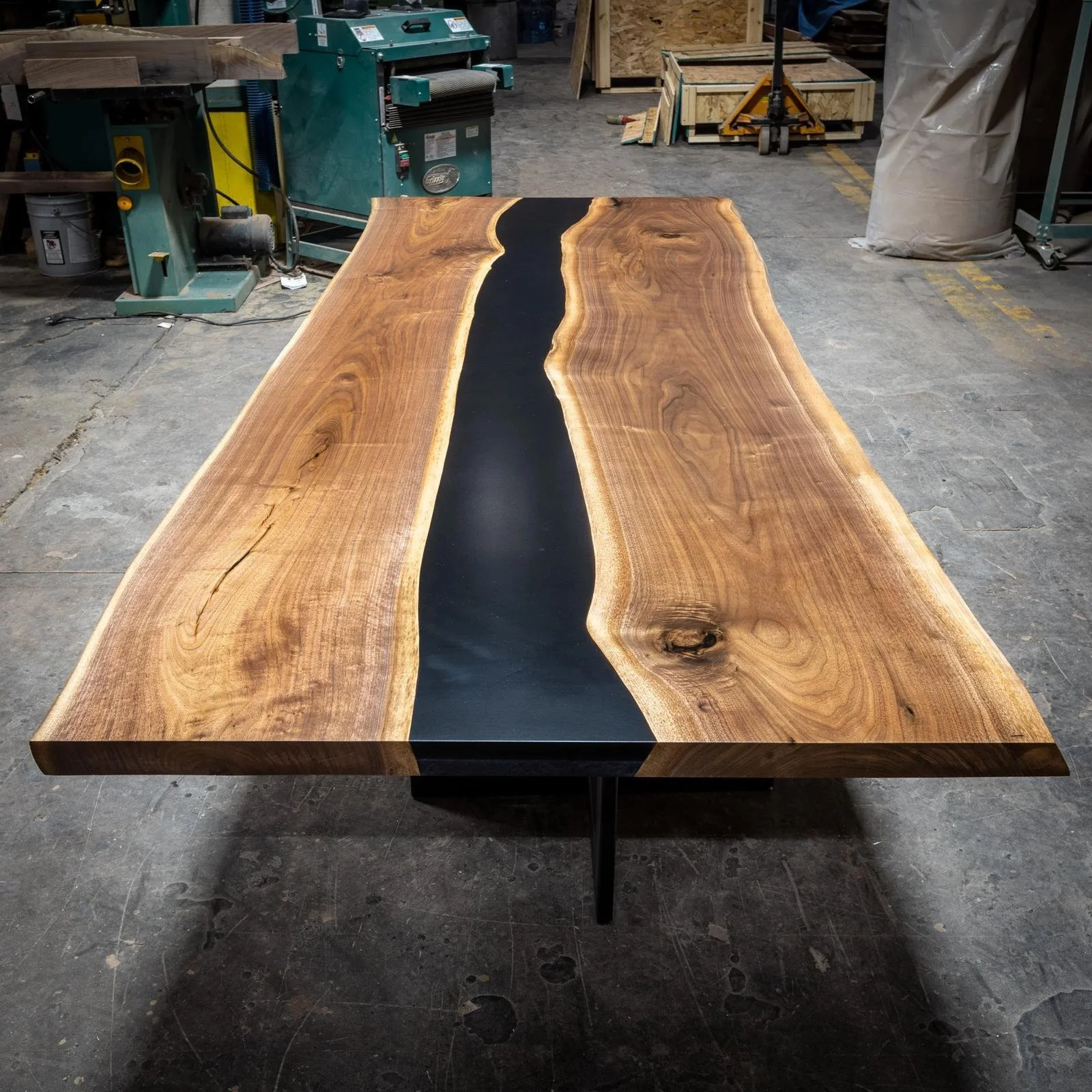 A wooden table with a natural wood finish and a black epoxy river running through the center in a workshop.