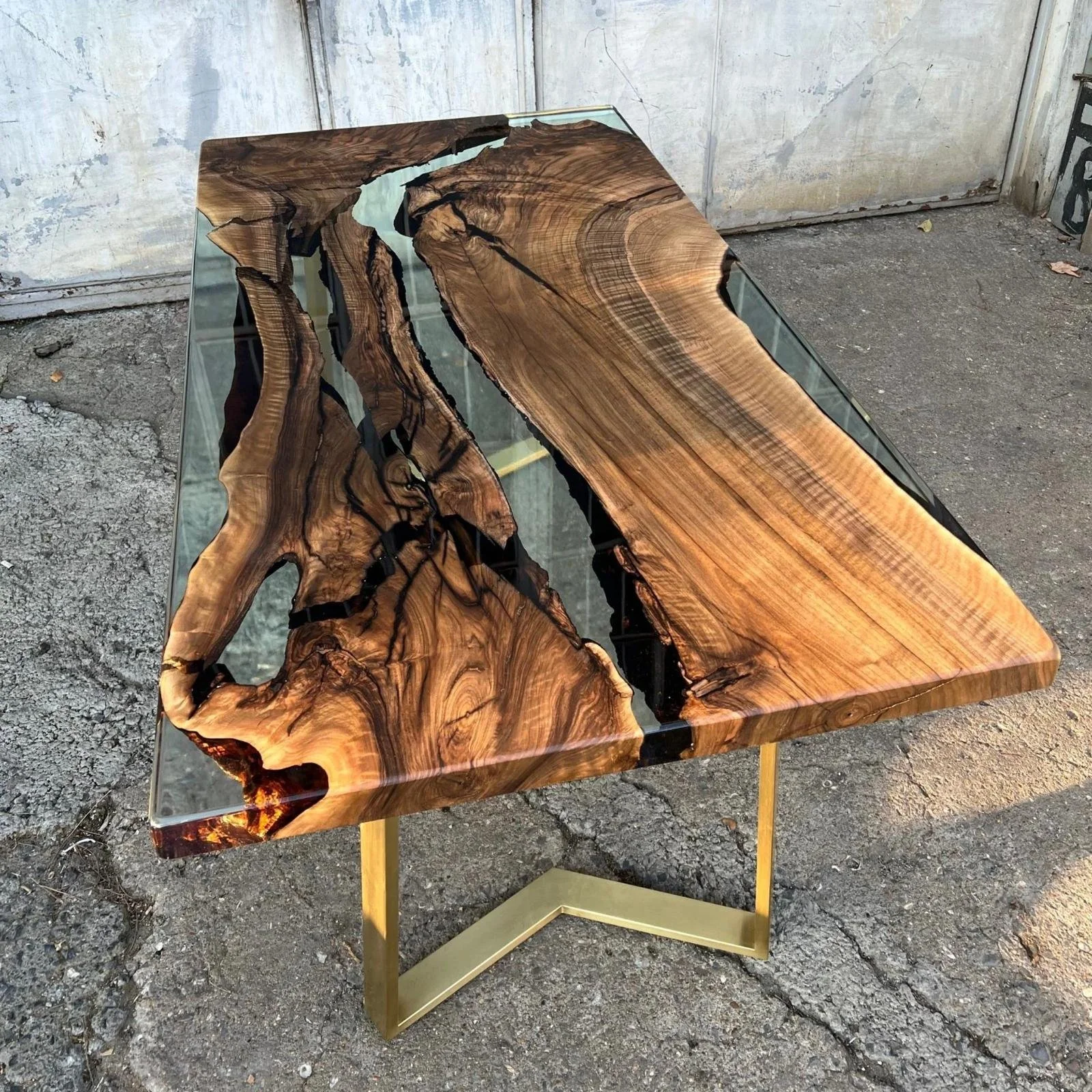 A table with a top made from a large, polished slab of natural wood with intricate grain patterns and a glossy finish, supported by a gold-colored metal frame.