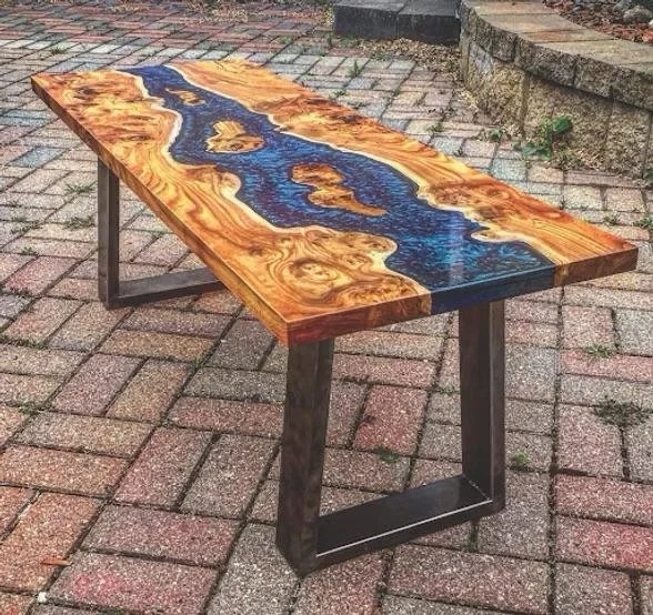 Wooden table with a natural wood and blue epoxy river design, standing on black metal legs on a brick patio.