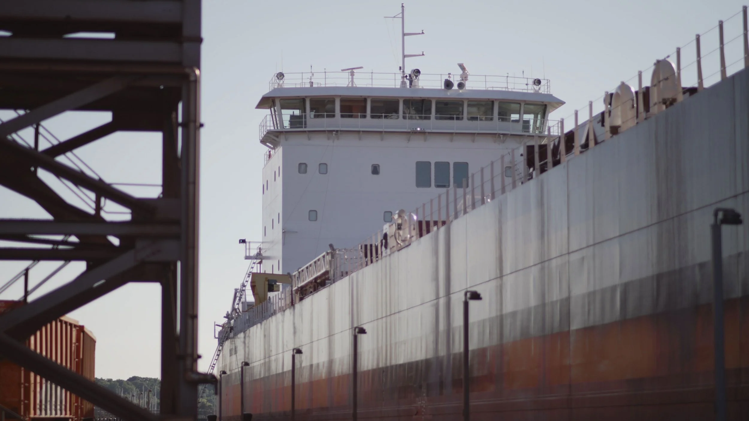 Pickands Mather 3PL Services | A large white cargo ship docked at a port, viewed from below with a portion of a metal staircase on the left side.