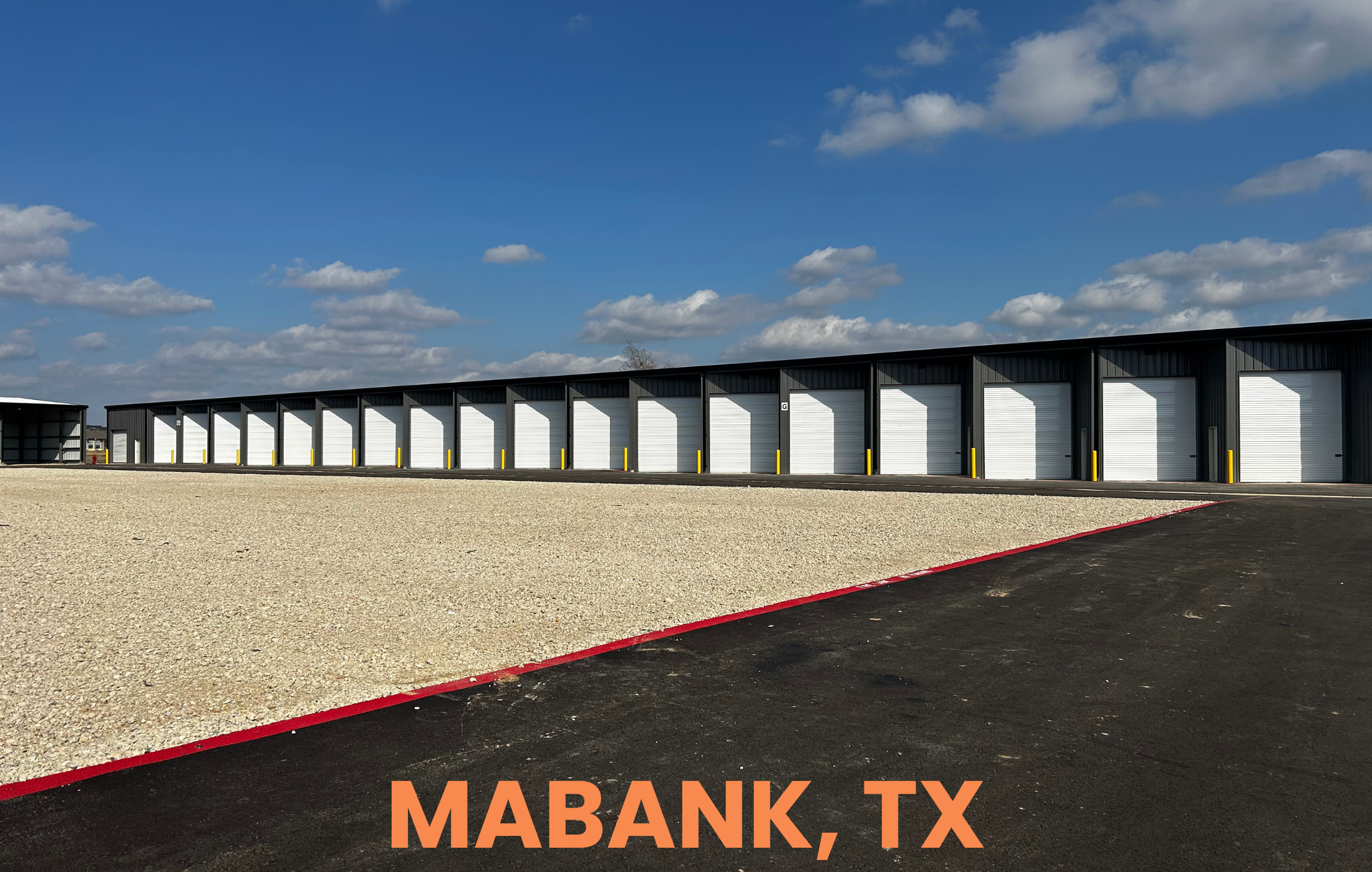Long row of storage units with white garage doors and black exterior walls, under a partly cloudy sky, in Mabank, Texas.