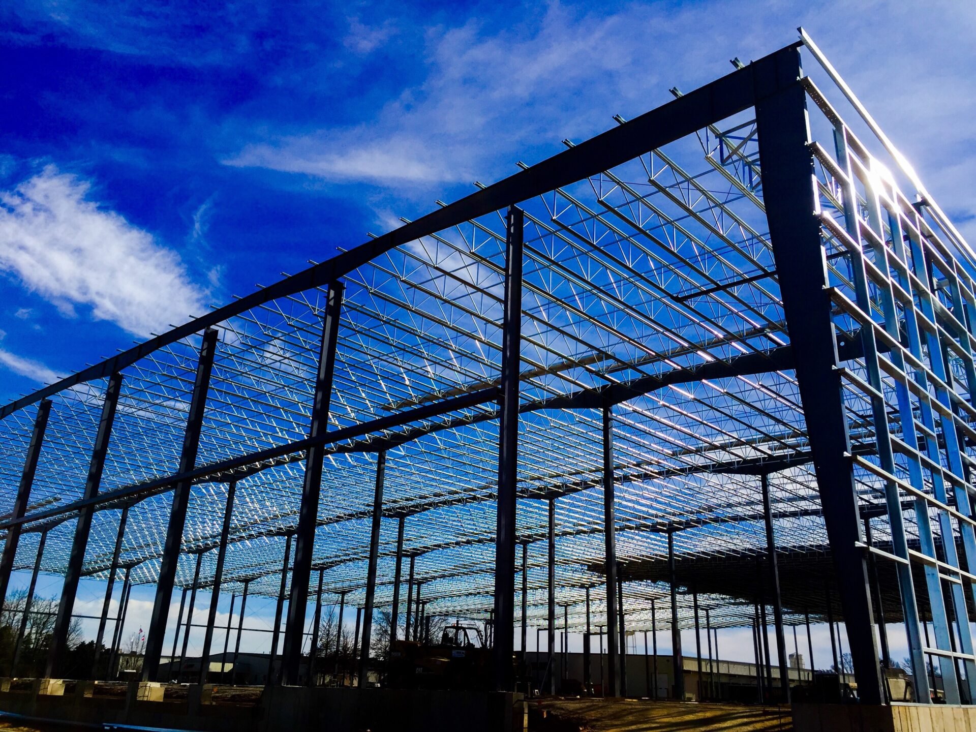 Steel framework of a building under construction with a blue sky and clouds in the background.