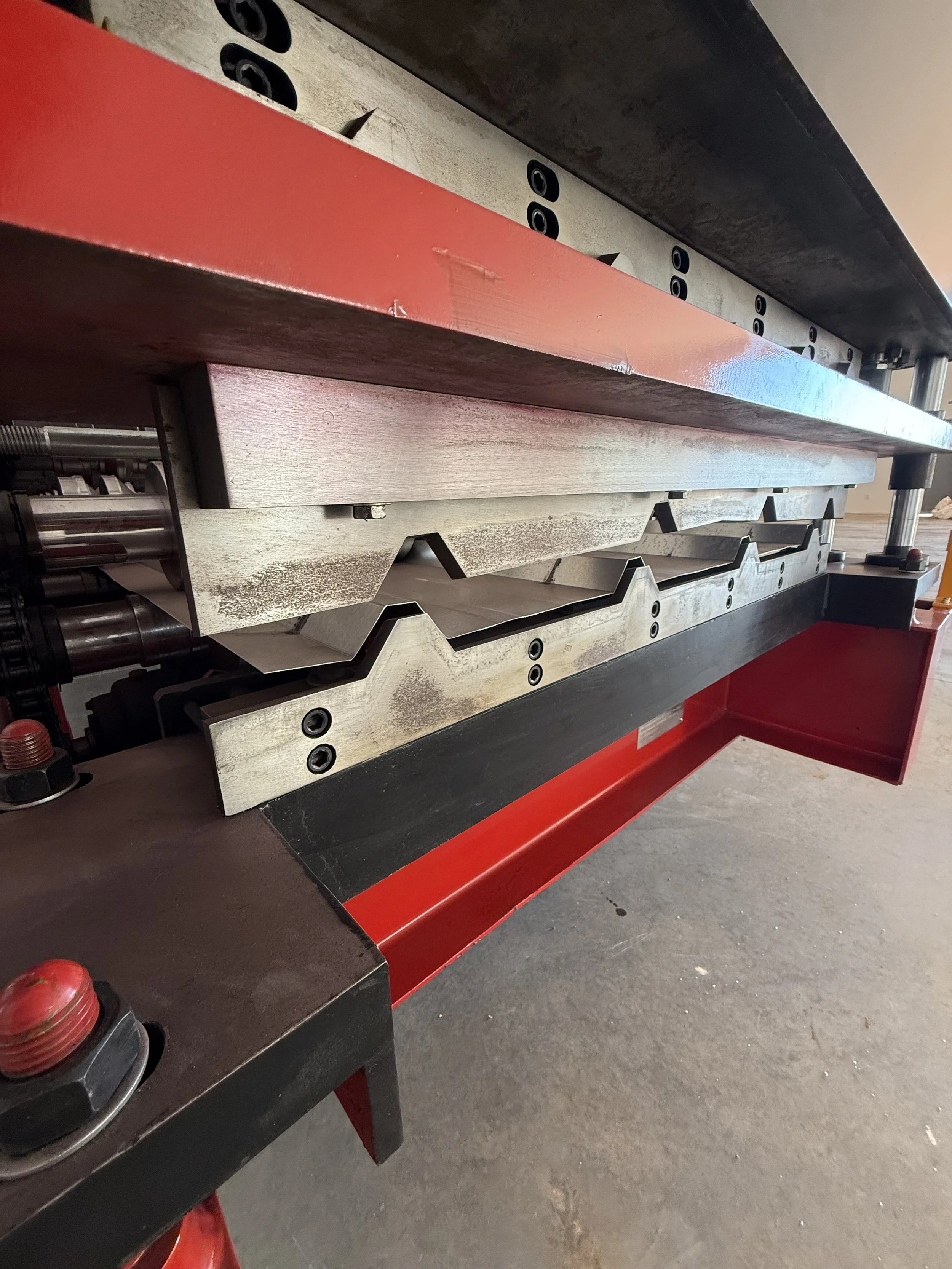 Close-up of a metal press machine with red and black framing, showing the pressing plates and mechanical components.