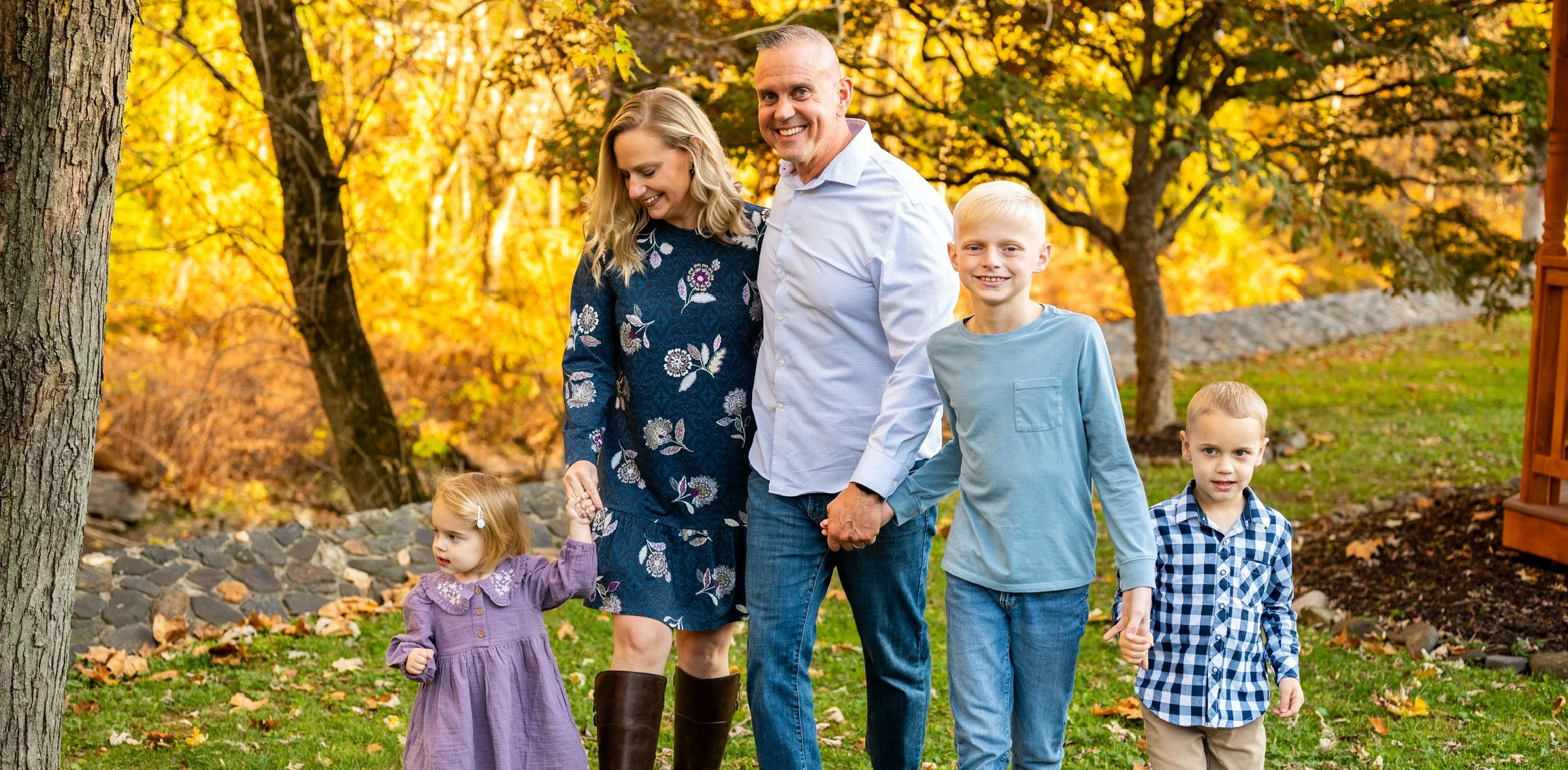 A happy family of five walking in a park during autumn, surrounded by colorful fall leaves and trees.