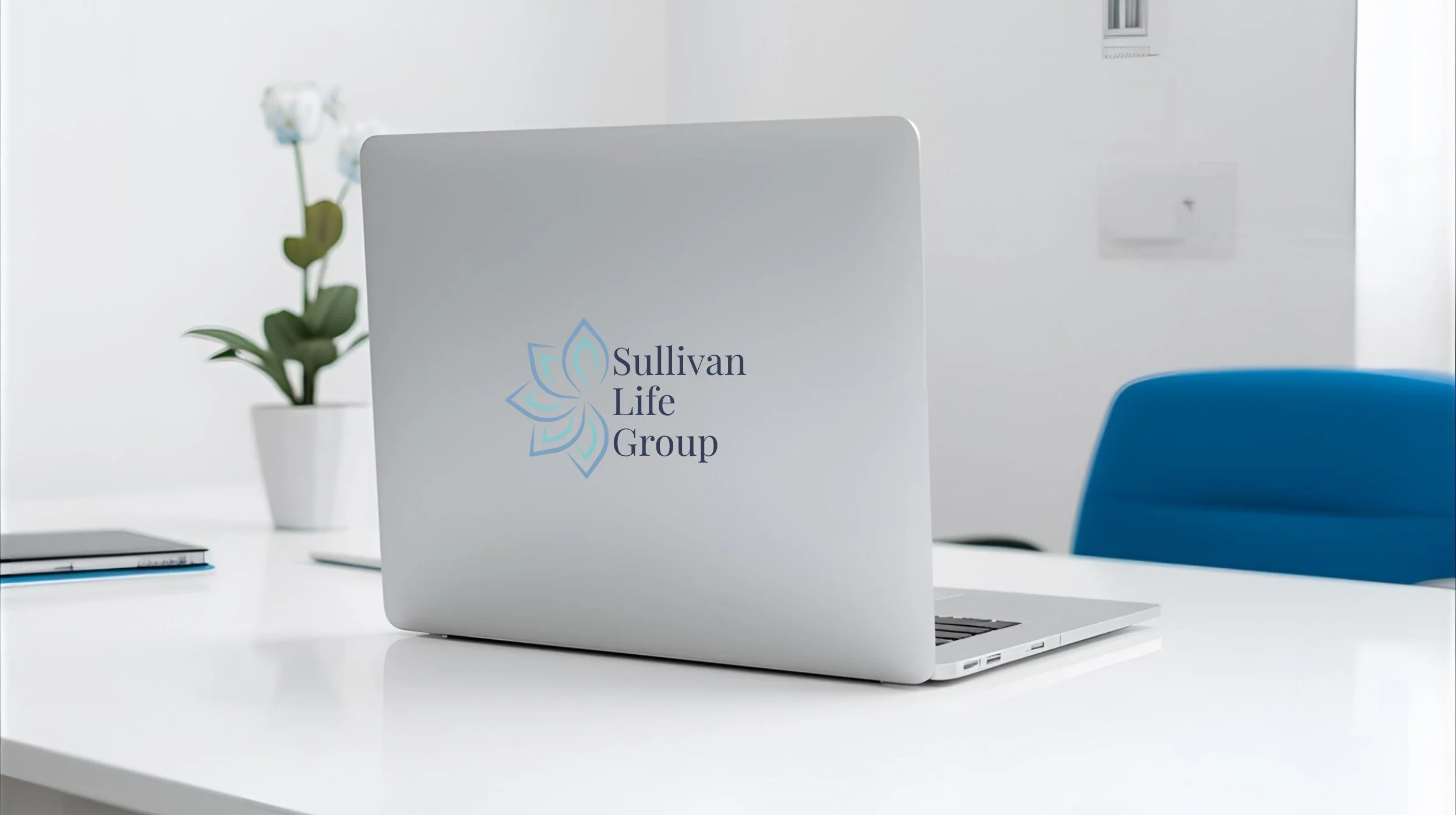 Laptop on white desk with Sullivan Life Group logo, a potted orchid, and a blue chair in the background.