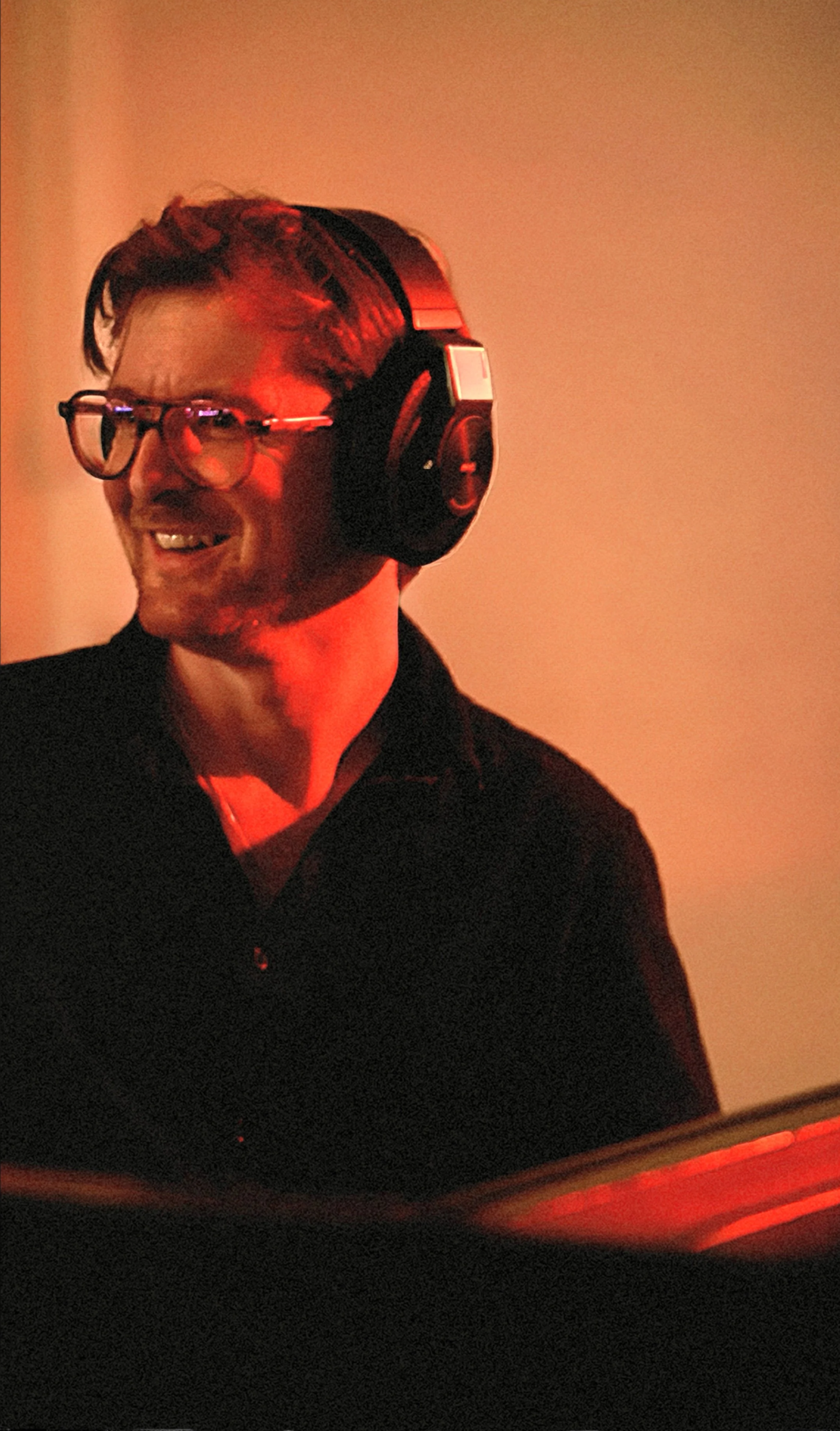 A man wearing glasses and headphones smiling in a warmly lit room.