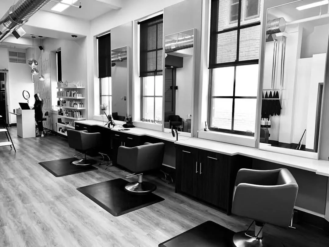 Modern salon or barbershop interior with styling stations, chairs, mirrors, and large windows in black and white.