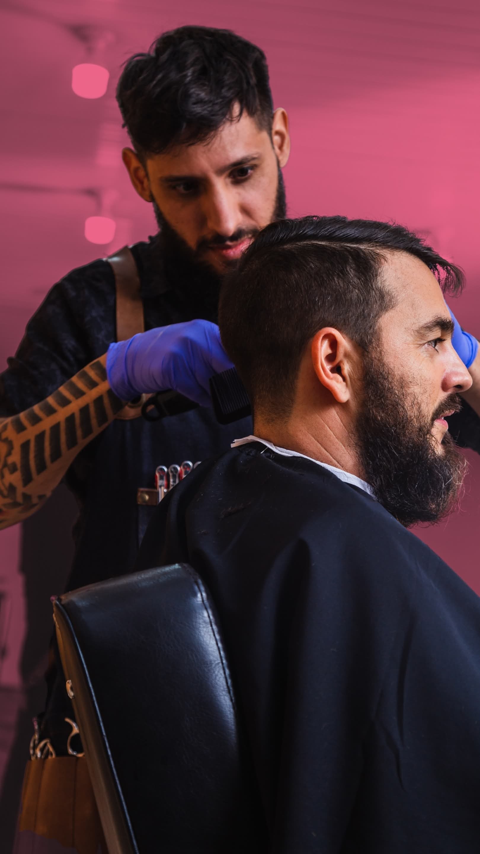 Barber cutting man's hair in a salon with pink lighting