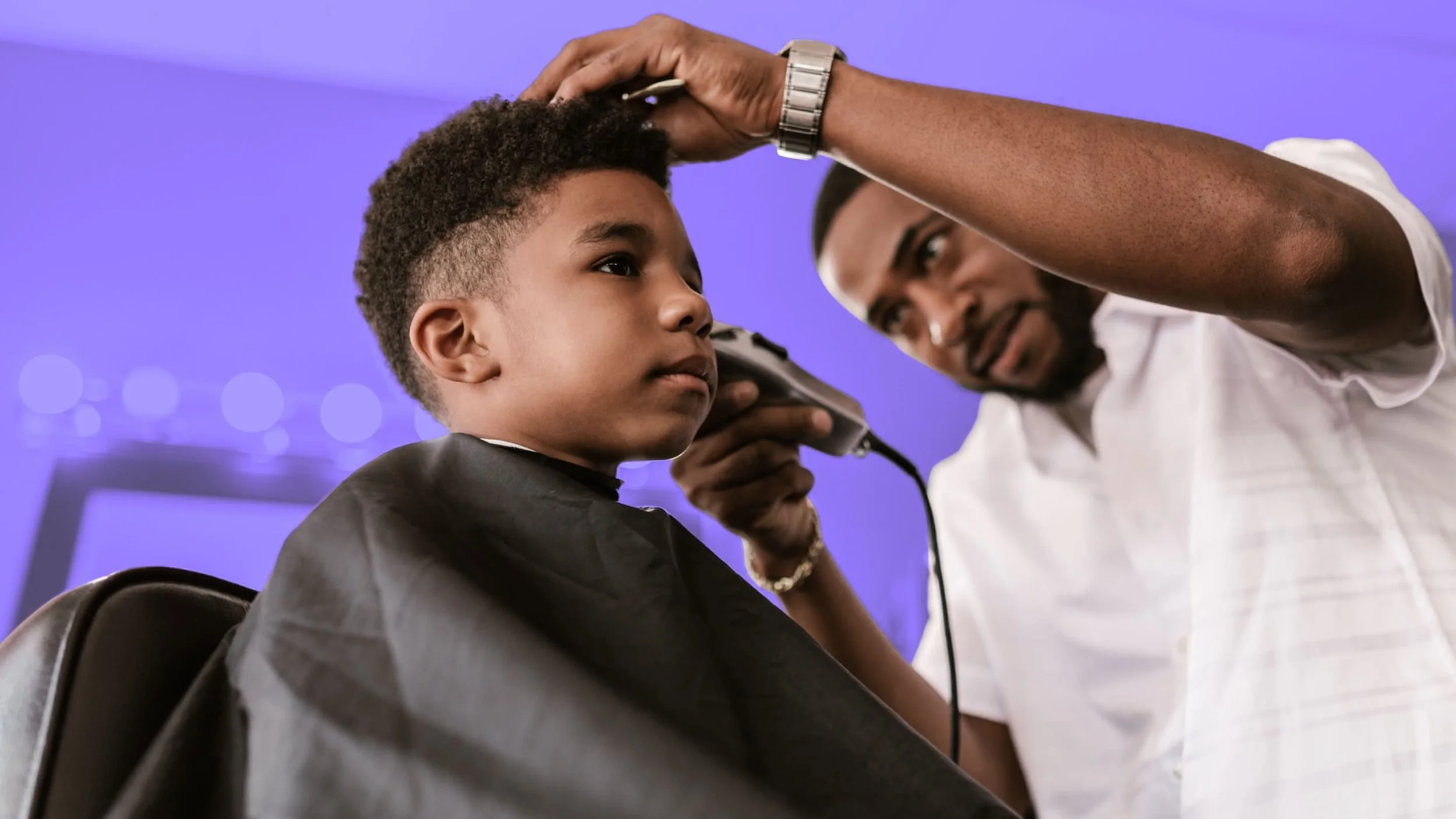 A young boy getting a haircut while a barber checks his haircut with a mirror.