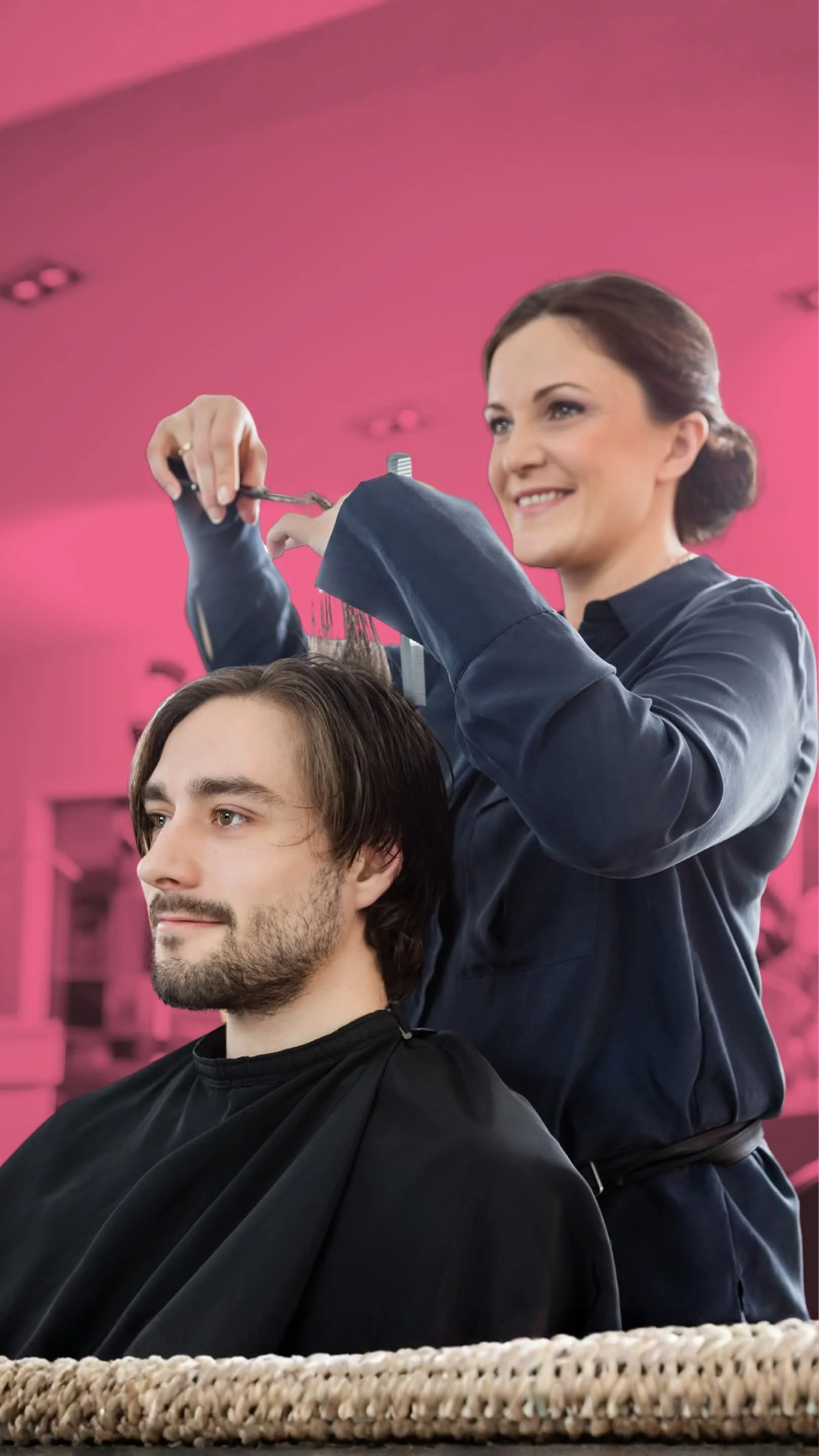 A woman is giving a man a haircut in a salon with a pink background.