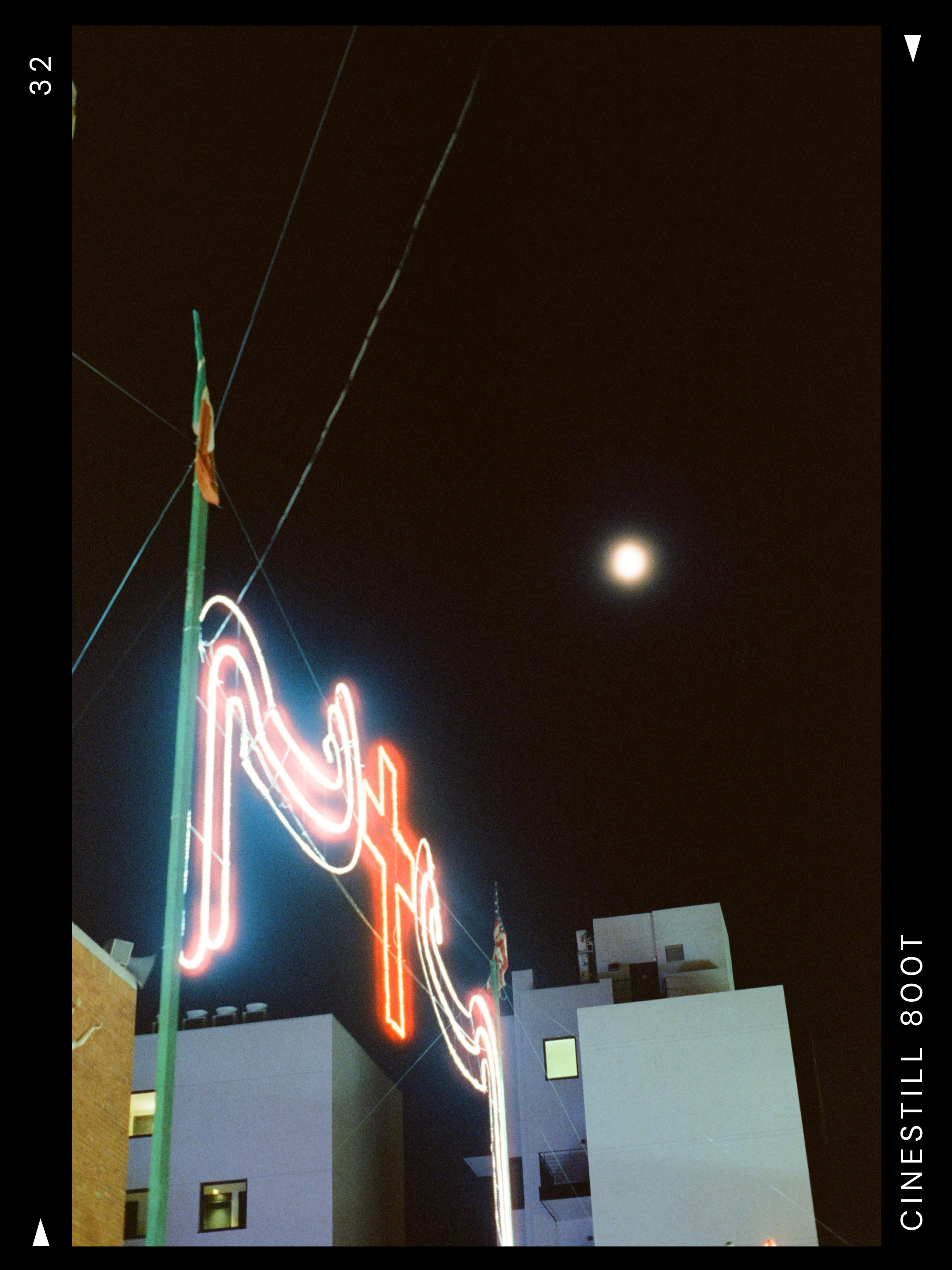 Night view of a neon sign on a building, with a bright moon in the dark sky.