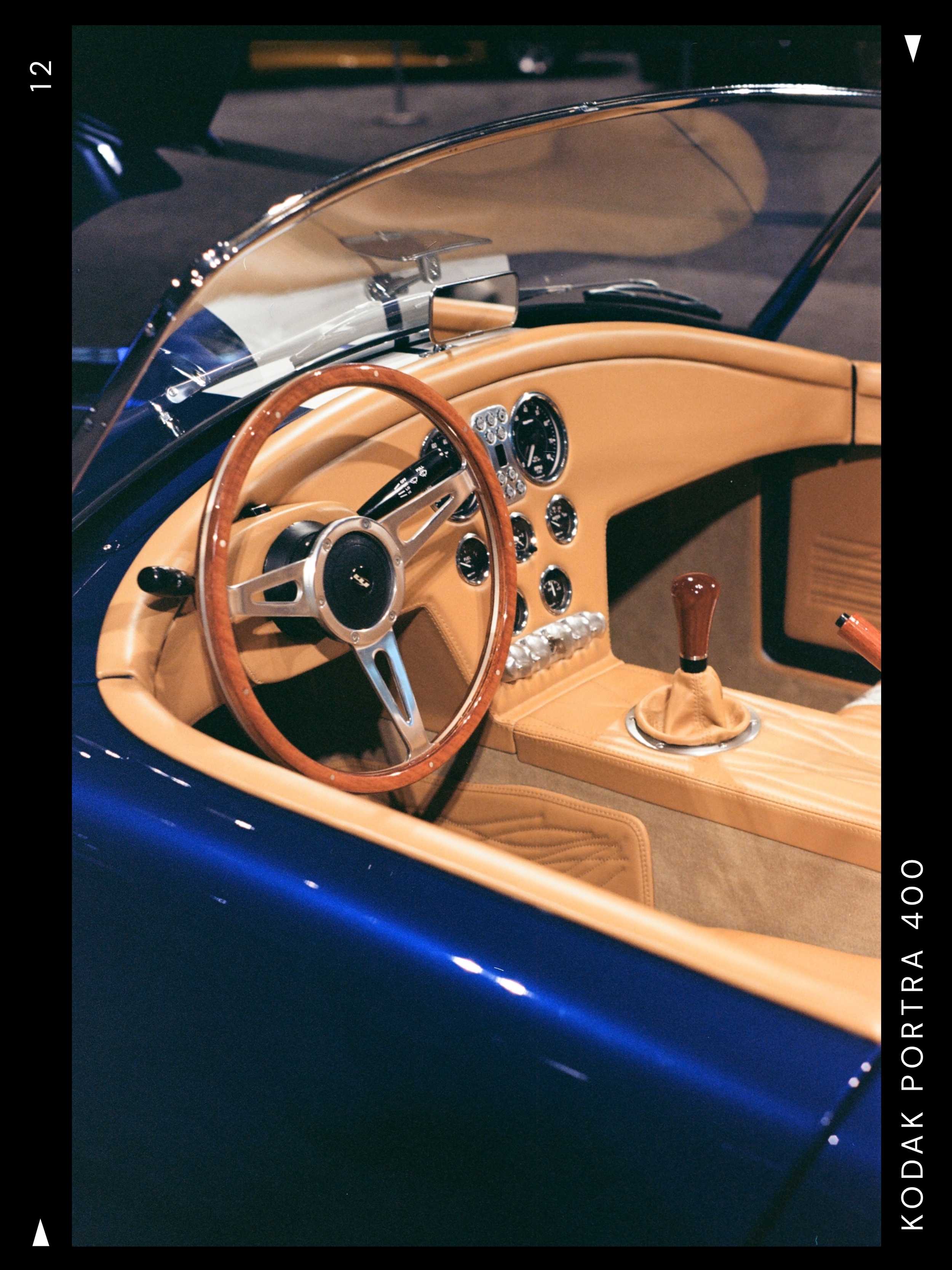 Interior of a vintage sports car with tan leather seats and dashboard, wooden steering wheel, and a gear shift lever.