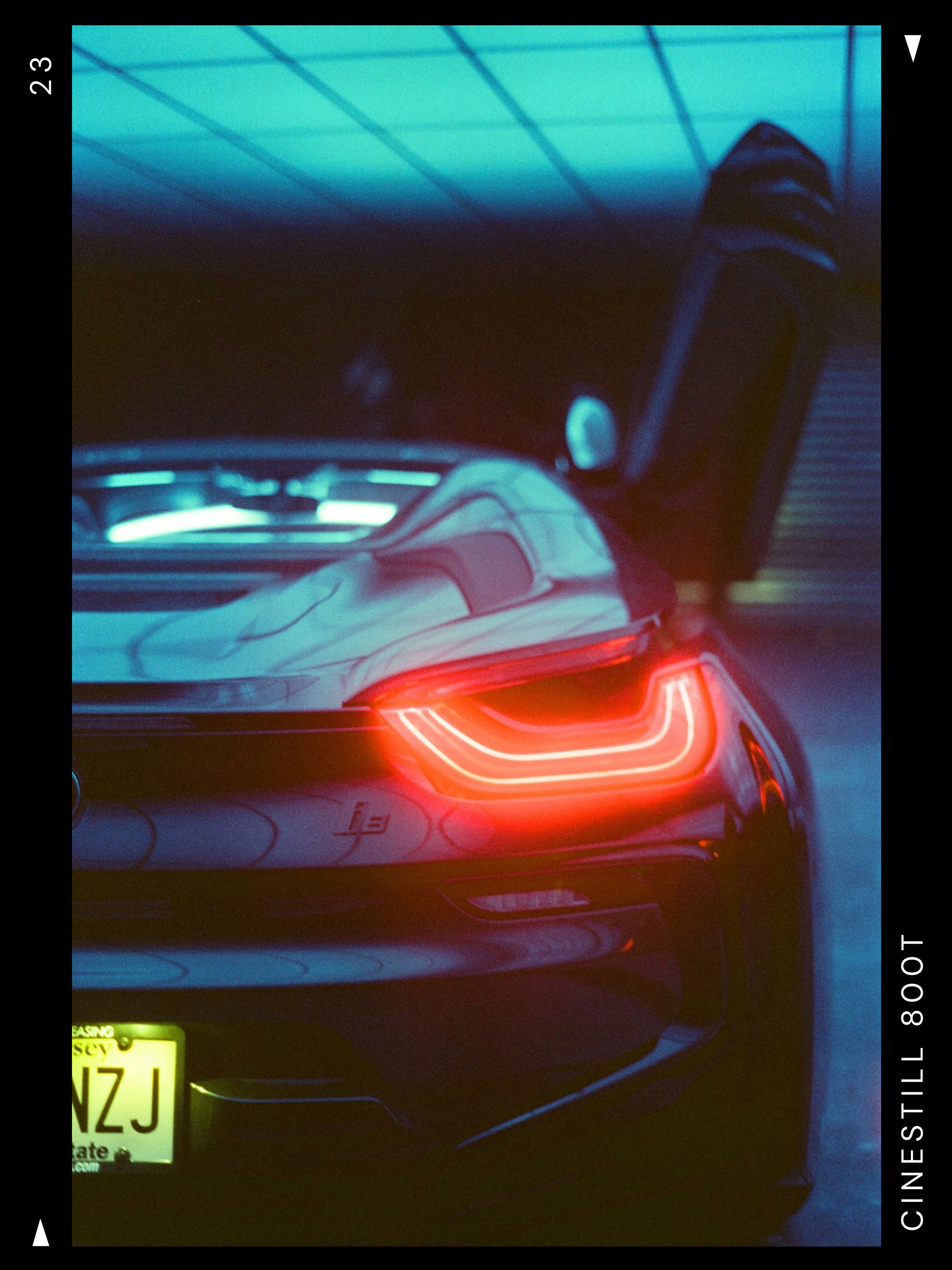Close-up of the rear of a sports car with illuminated LED taillights, showing a New Jersey license plate, in a dimly lit garage or tunnel with blue lighting.