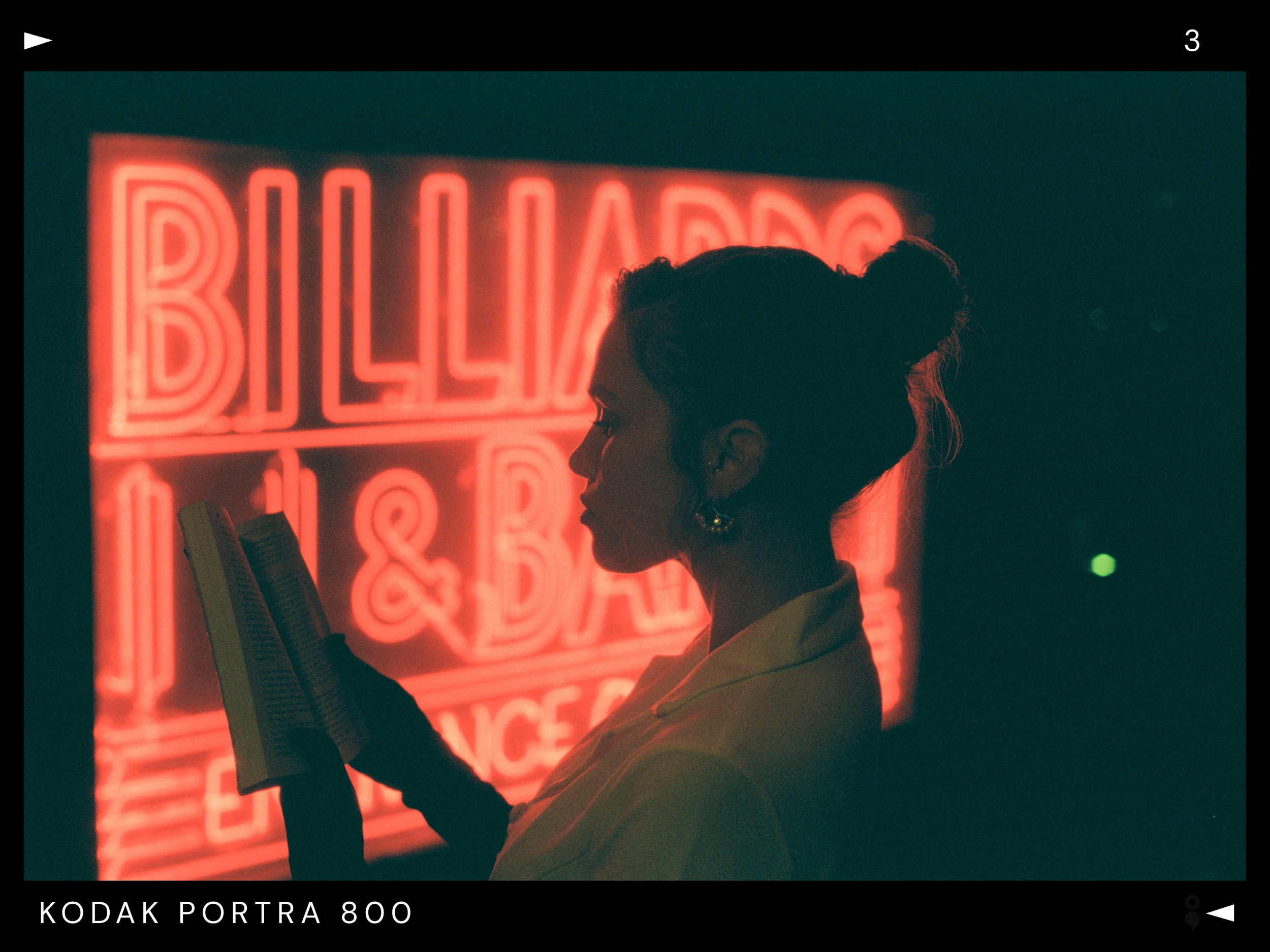 Silhouette of a woman reading a book at night with a red neon sign reading 'BILLIARD & BAR' in the background.