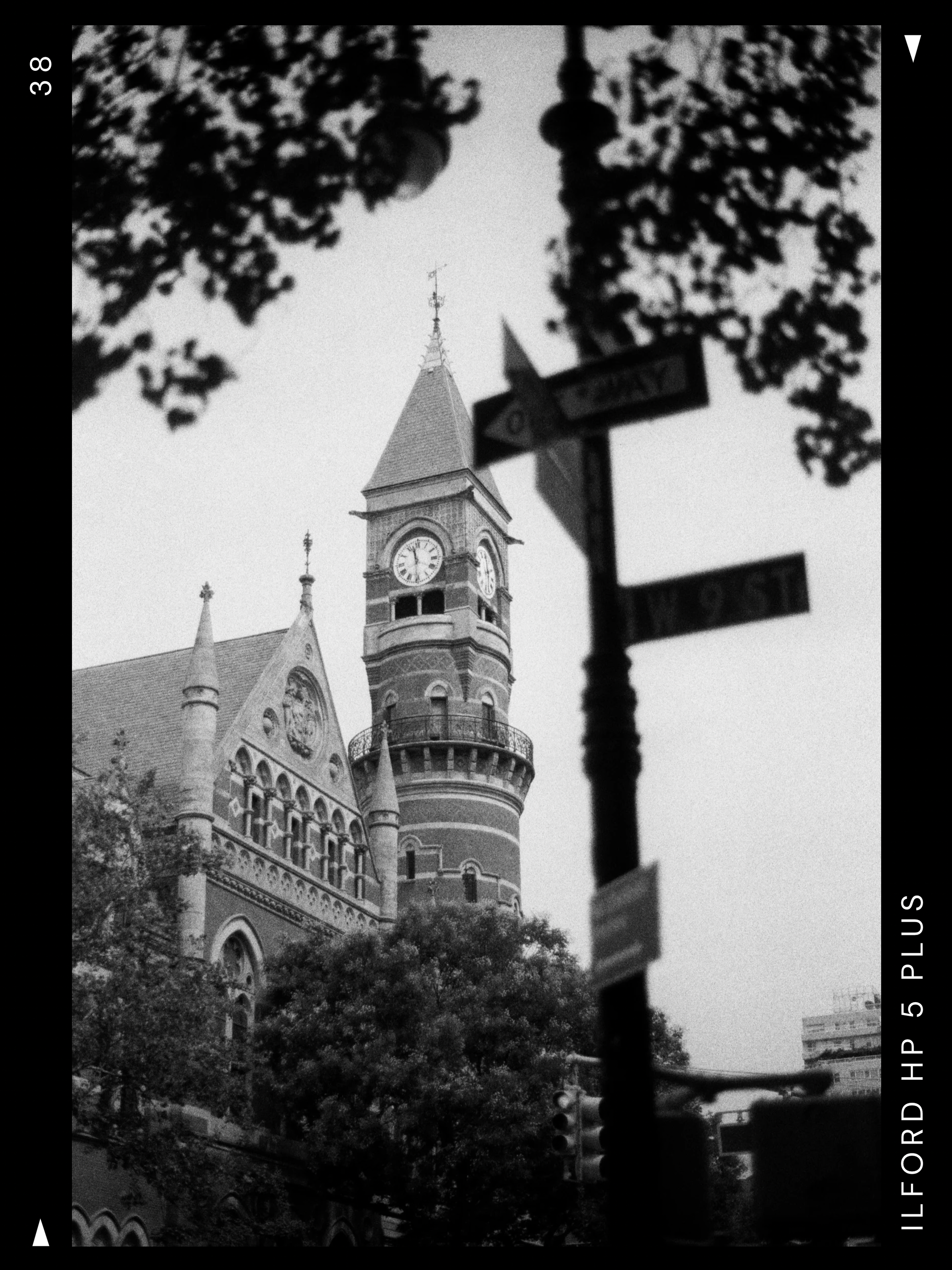 Black and white photo of a historic castle with a clock tower, partly obscured by a street sign and trees.