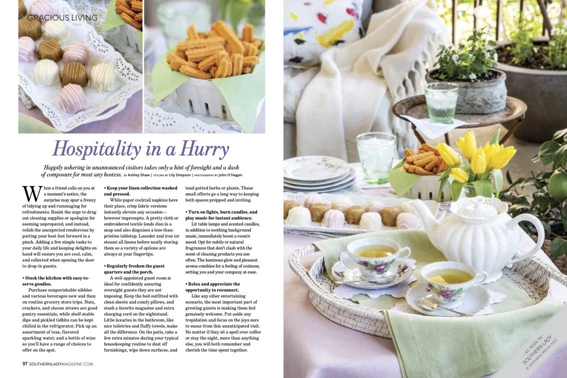 A magazine spread showing a table set with a teapot, teacups, and saucers with tea, surrounded by a lush garden. The table has a cloth, and there are plates of snacks including churros and cupcakes.