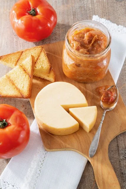 Cheese, toast, and tomato with a jar of apple butter on a wooden board.