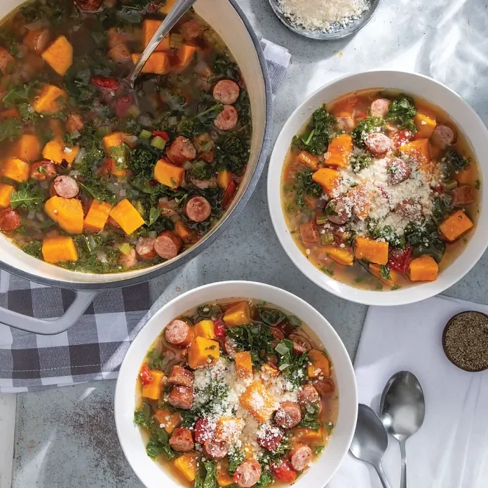 Three bowls of vegetable soup with sausage, topped with grated cheese, served on a table with spoons and a jar of pepper.