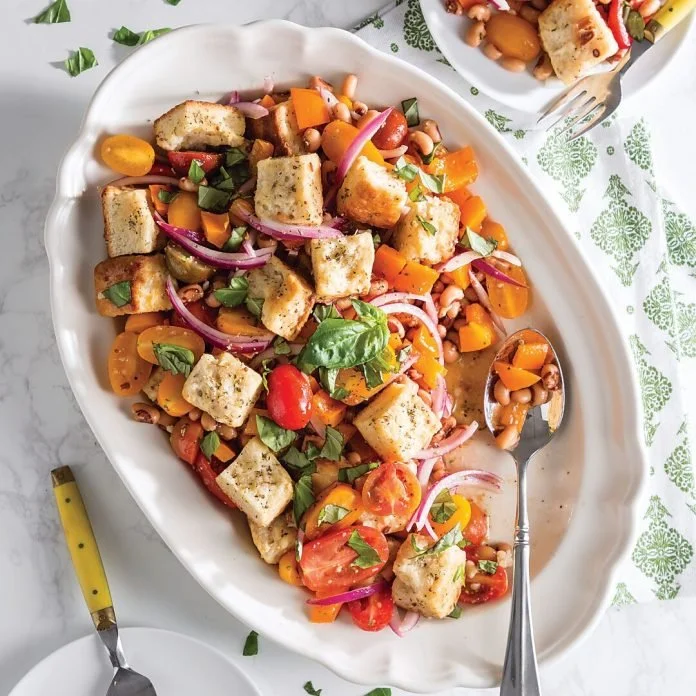 Vegetarian salad with grilled tofu, cherry tomatoes, bell peppers, red onions, chickpeas, and fresh herbs served on a white platter.