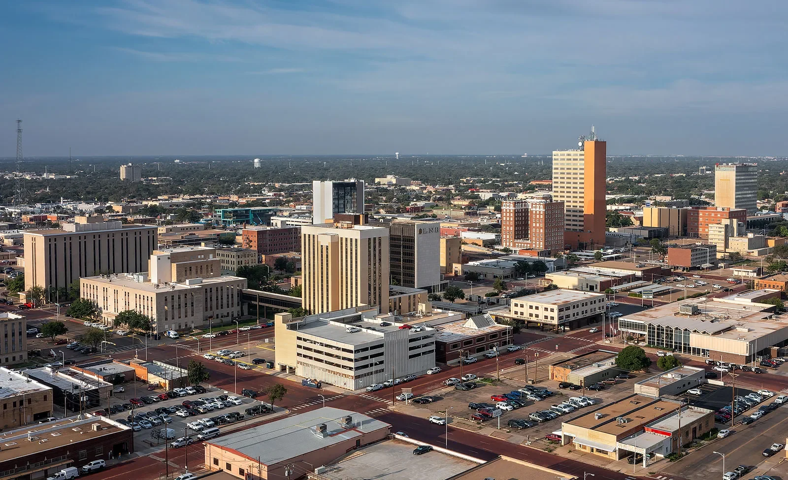 A cityscape view of downtown with various tall buildings, parking lots, and streets extending to the horizon under a partly cloudy sky.