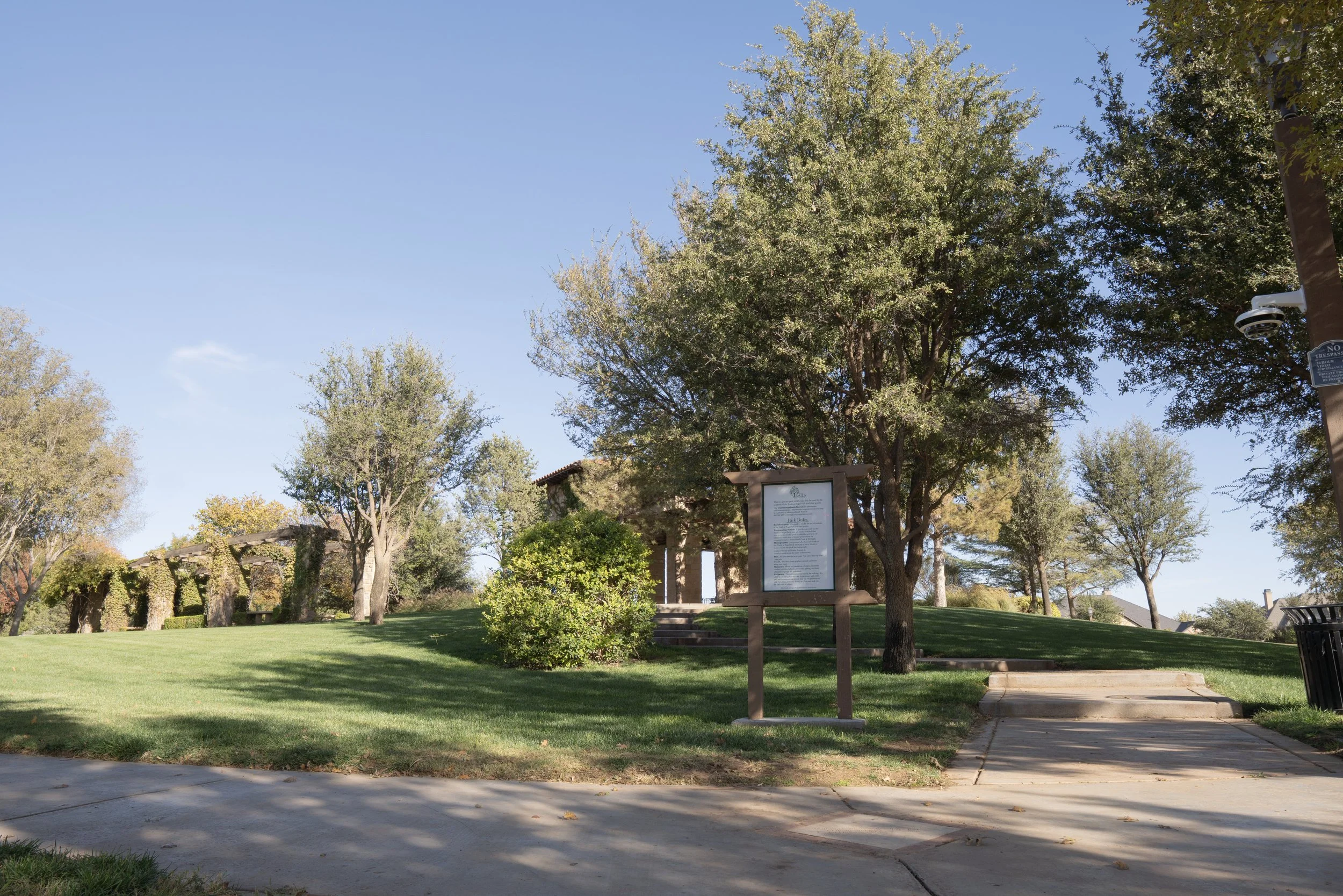 A scenic park scene with green grass, trees, and a stone building in the background under a clear blue sky.