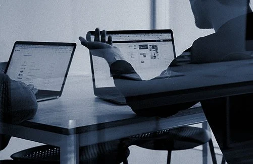 A person explaining or discussing something with two laptops open on a table.