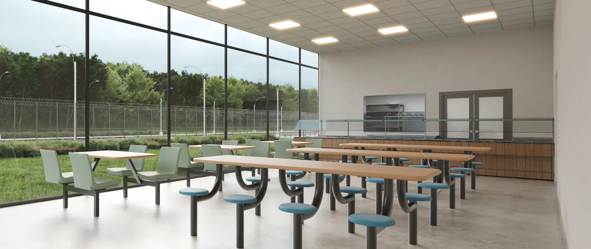 Empty cafeteria with large windows, wooden tables with attached blue and green chairs, outdoor view of trees and a fence.