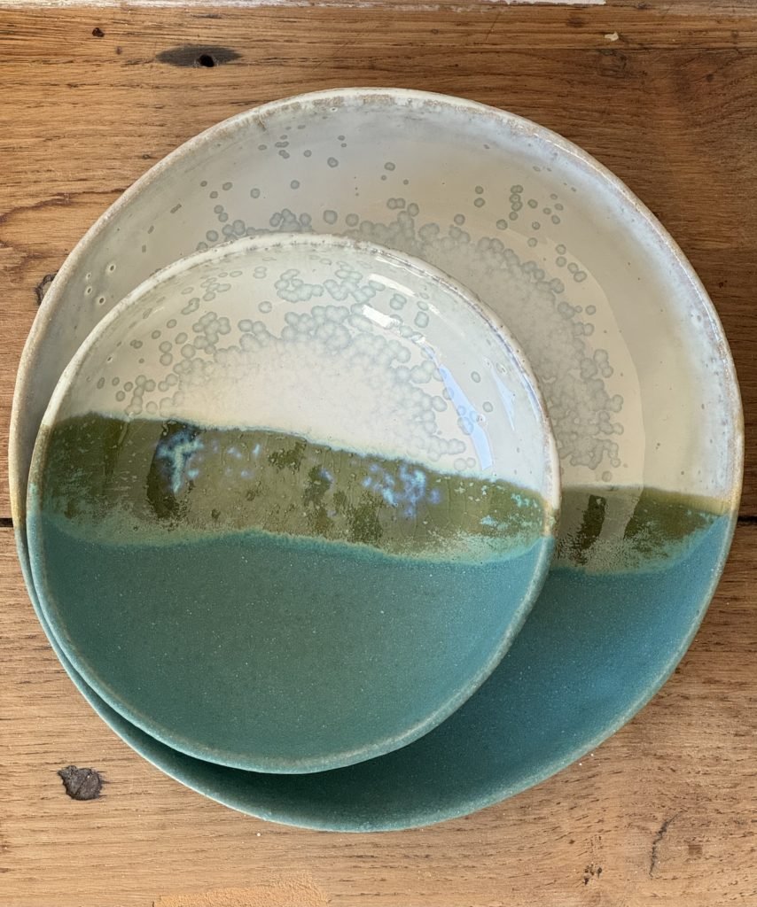 Deux assiettes en céramique de différentes tailles, avec un motif bleu vert à l'intérieur, posées sur une surface en bois.