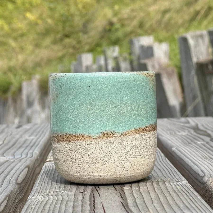 Une tasse en céramique sur une table en bois, avec un fond flou de nature
