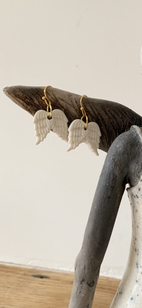 Boucles d'oreilles en forme d'ailes d'ange suspendues à une branche en bois.