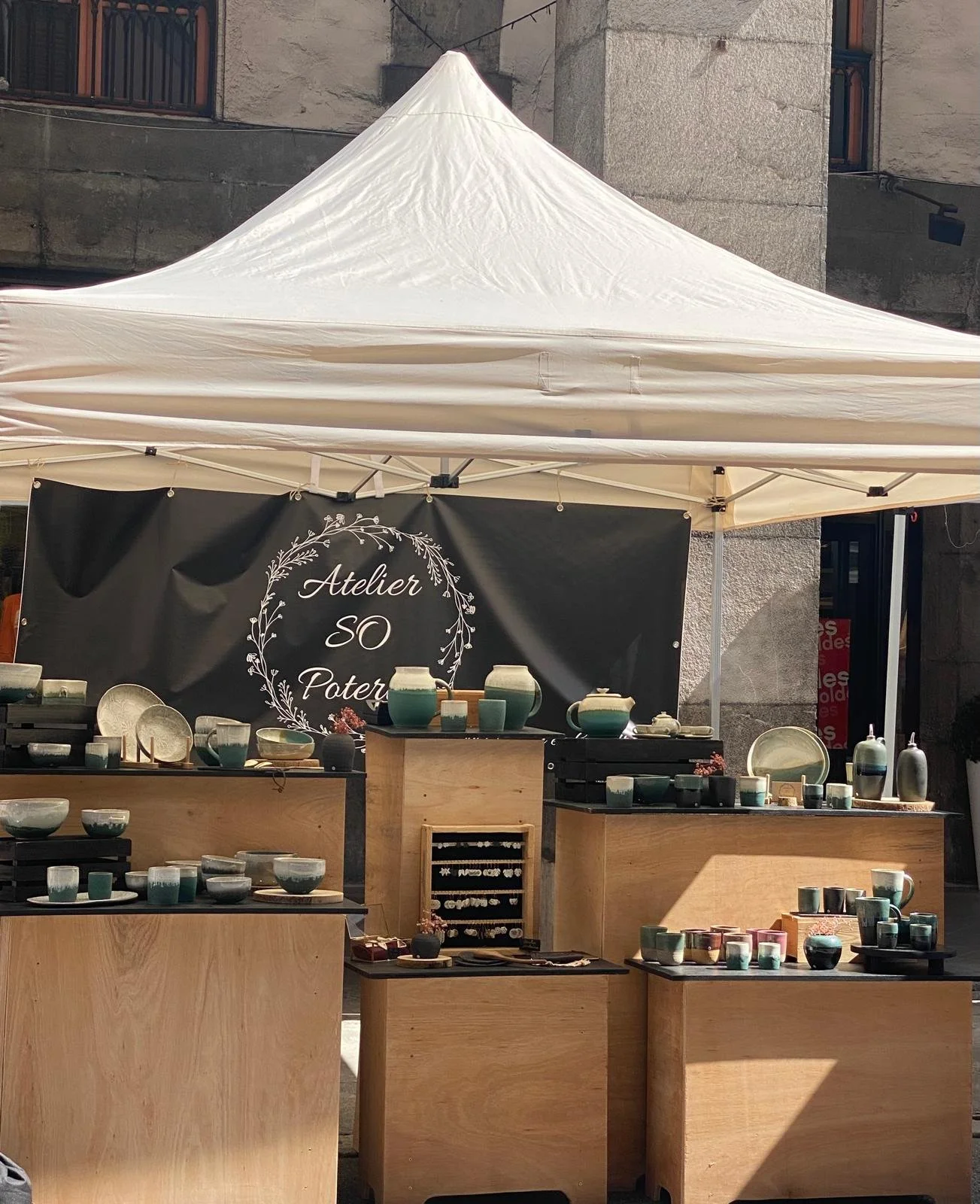 Stand de vente de poteries artisanales sous une tente blanche, avec une bannière indiquant 'Atelier SO Poter'.