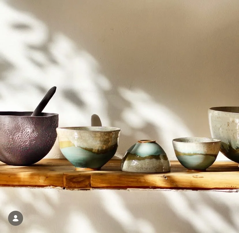 Une rangée de bols en céramique de différentes tailles et couleurs posés sur une planche en bois, avec des ombres et des reflets de lumière.