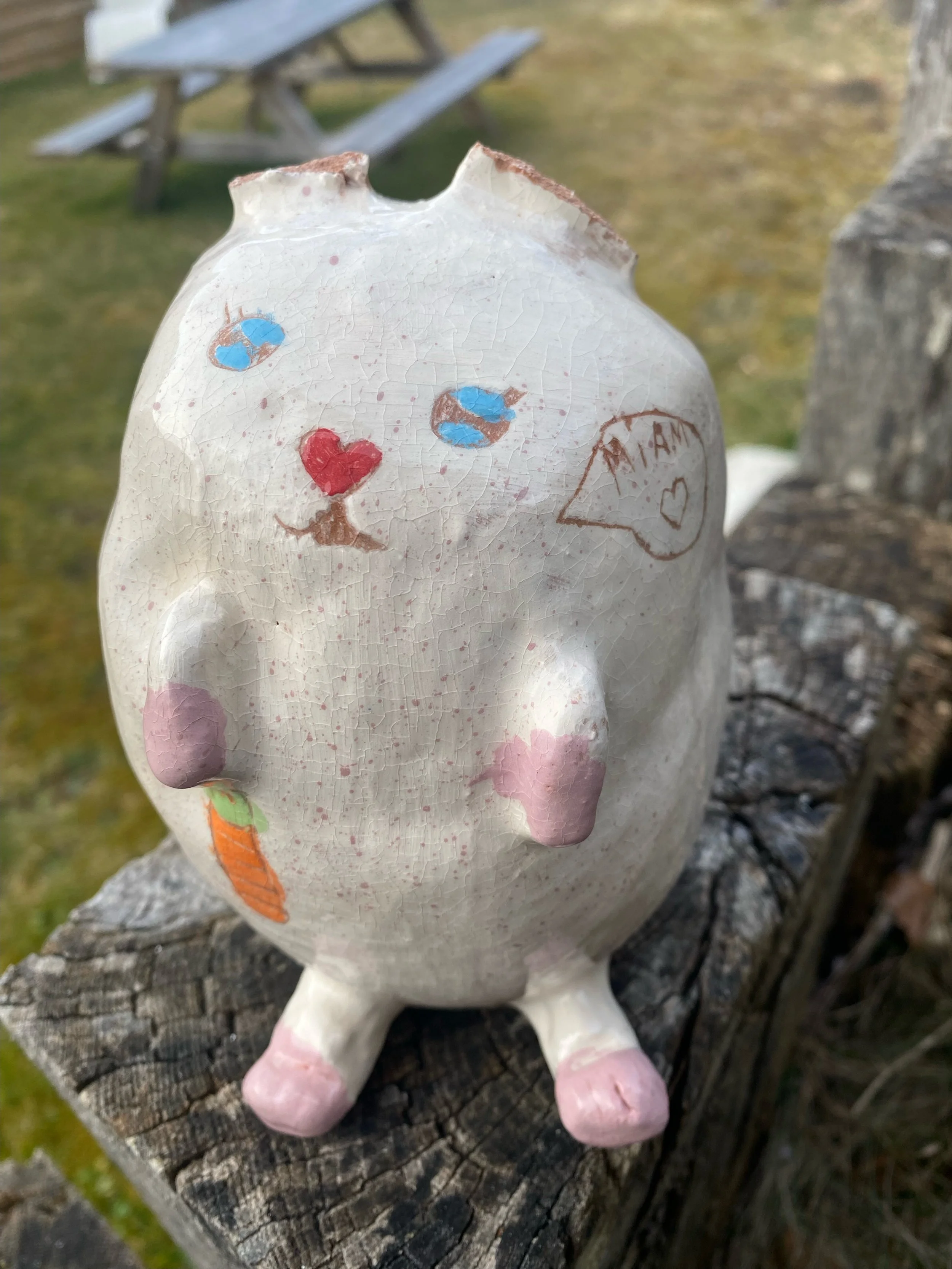 Une figurine en forme de chat avec un visage rond, des couleurs pastel, et un dessin de cœur dans une bulle de dialogue avec le mot "MIAM" écrit à l'intérieur.