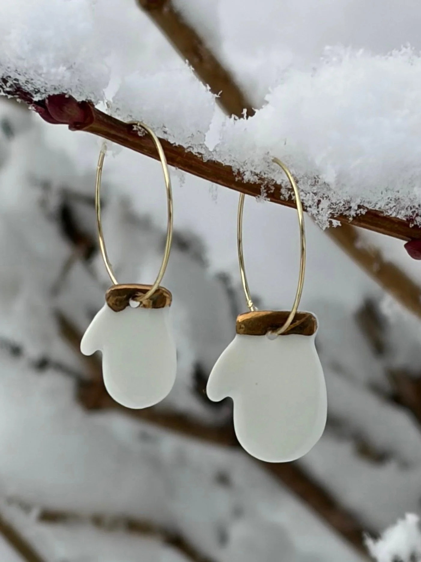 Boucles d'oreilles en céramique en forme de moufle suspendues à une branche enneigée.