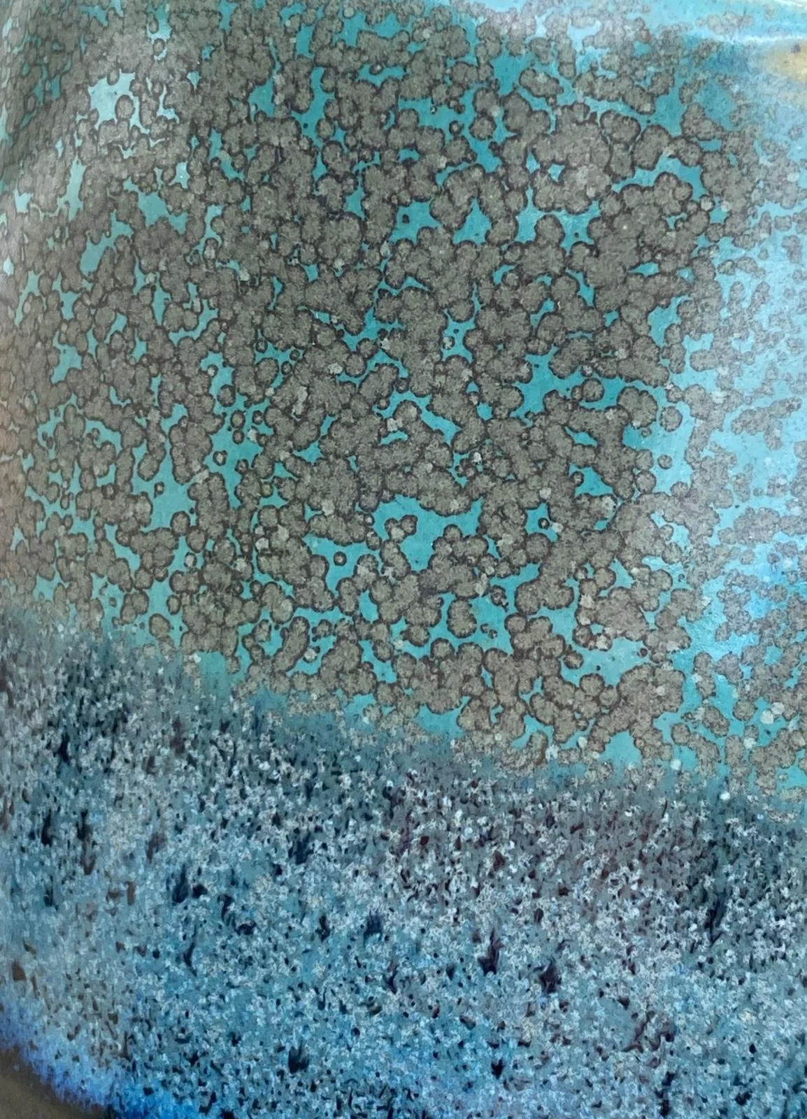 Détail d'une surface en grès permettant de voir les motifs noirs et bleus que la cuisson à permis de créer.