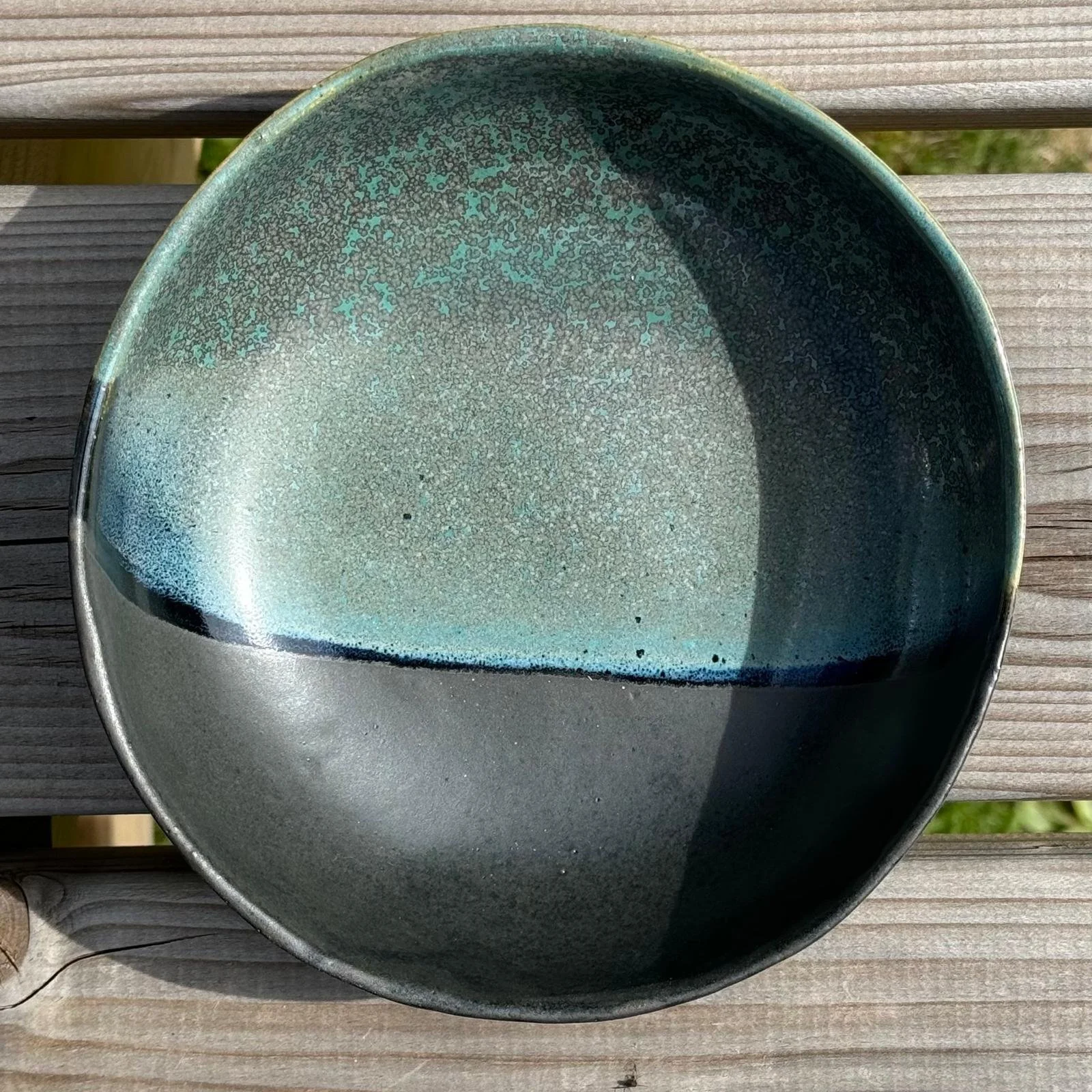 Assiette en grès avec un design teinté de nuances de vert et de gris, posée sur une surface en bois.