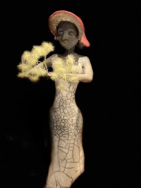 Statue d'une femme avec un chapeau rouge et des fleurs jaunes, fond noir. Réalisé avec la technique "Raku"