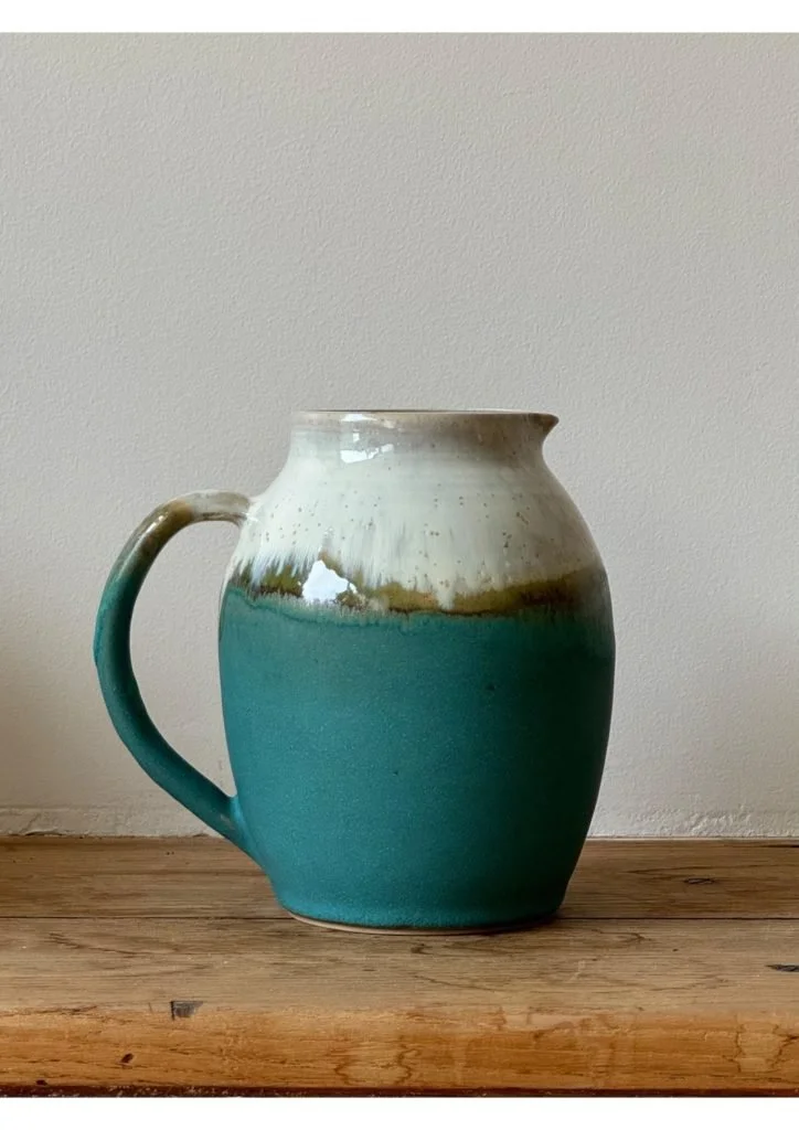 Une cruche en céramique avec un dégradé de couleurs allant du blanc en haut au vert en bas, posée sur une surface en bois.