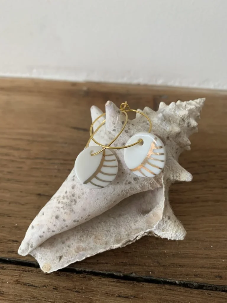Des boucles d'oreilles en or stylisées posées sur une coquille d'escargot, le tout placé sur une planche en bois.