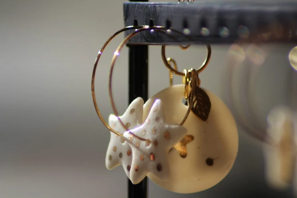Boucles d'oreilles pendantes en céramiques avec des étoiles en or sur un fond blanc avec un cercle en or