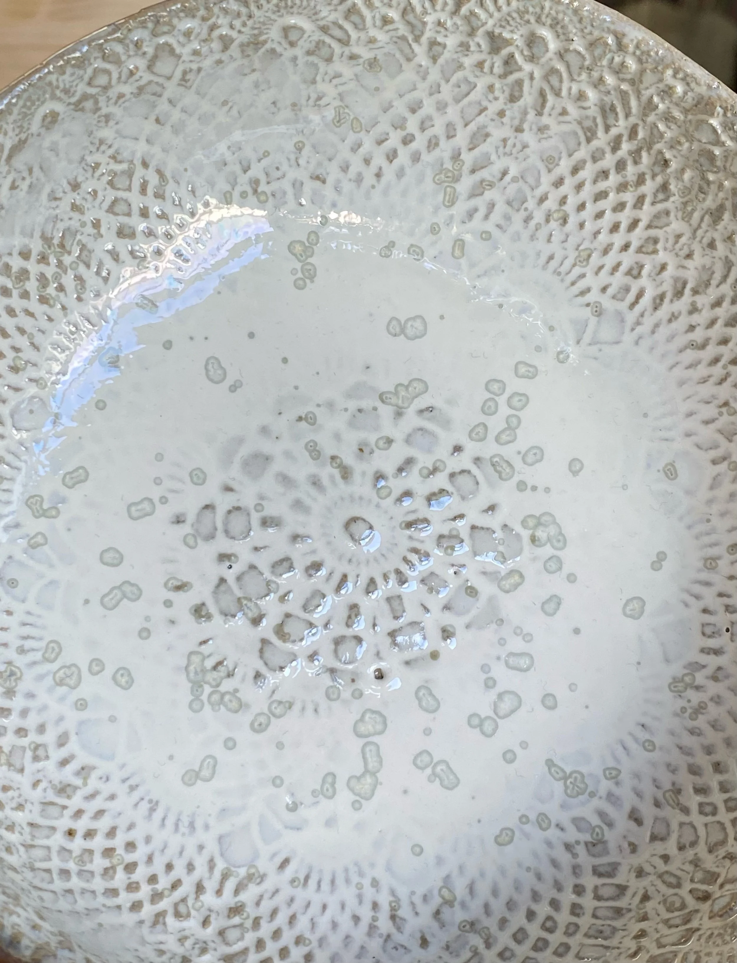 Un plateau en verre ou en céramique avec un motif décoratif en forme de mandala ou de fleur, la surface est lisse et transparente avec quelques reflets lumineux.