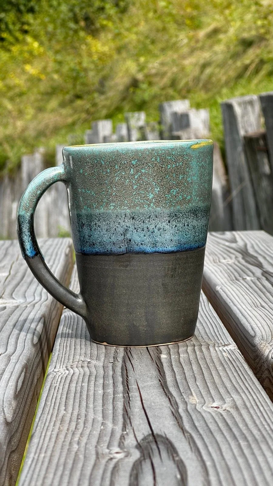 Tasse en céramique avec une finition dégradée de couleurs vertes, bleues et noires, placée sur une table en bois.