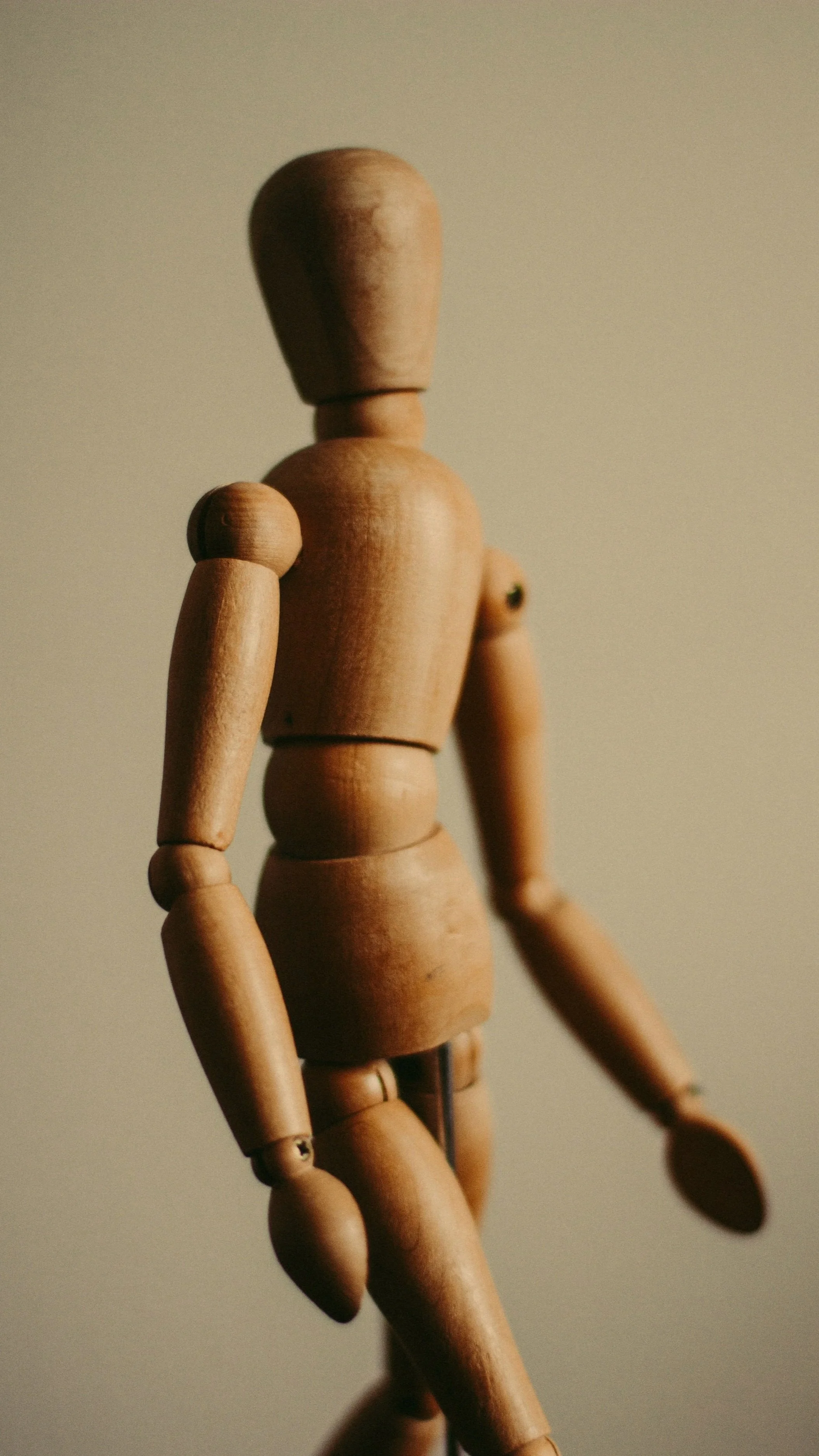 A close-up of a wooden artist mannequin with outstretched arms against a plain background.