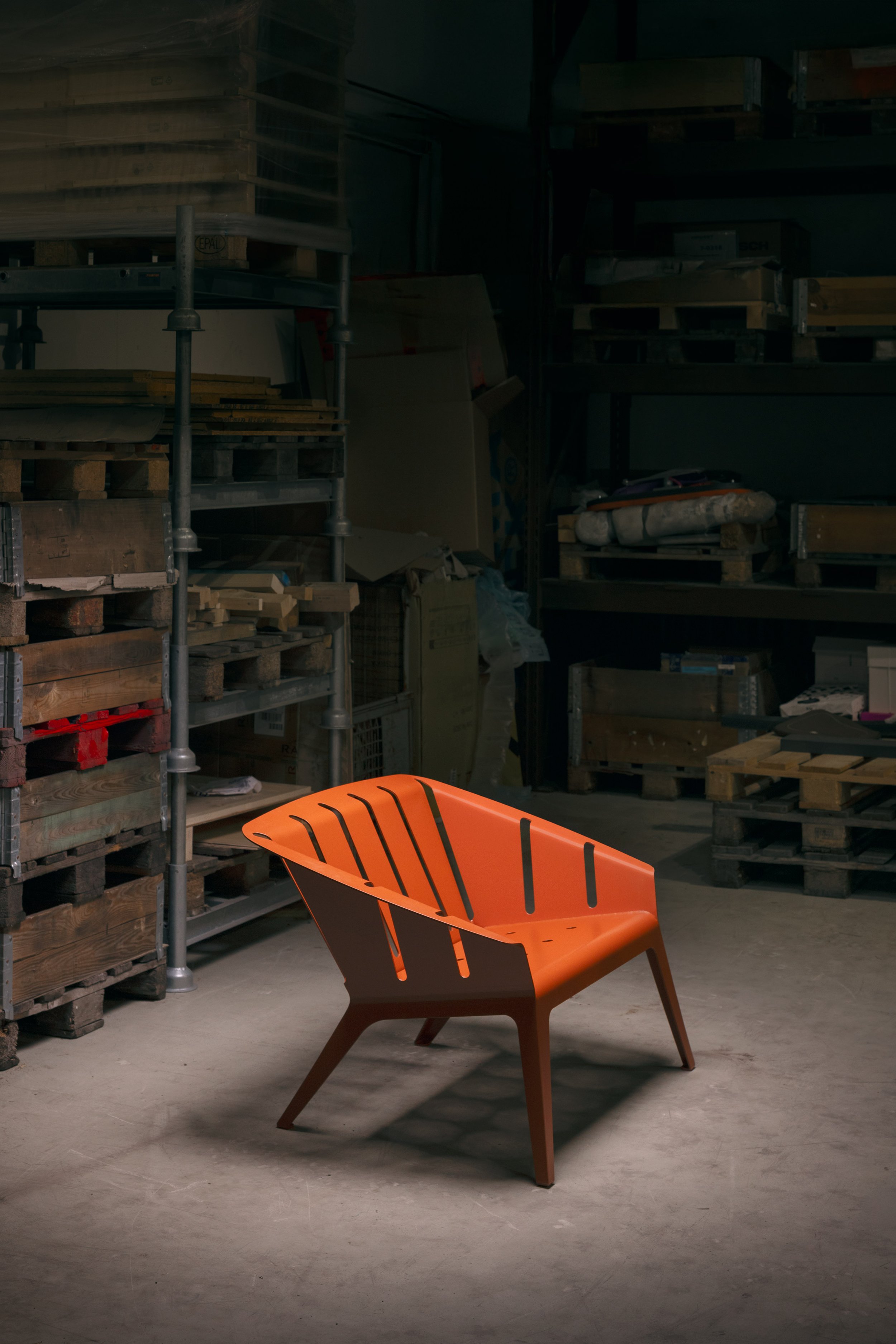 Ein orange farbener Stuhl in einem Lagerraum mit Holzpaletten und Regalen