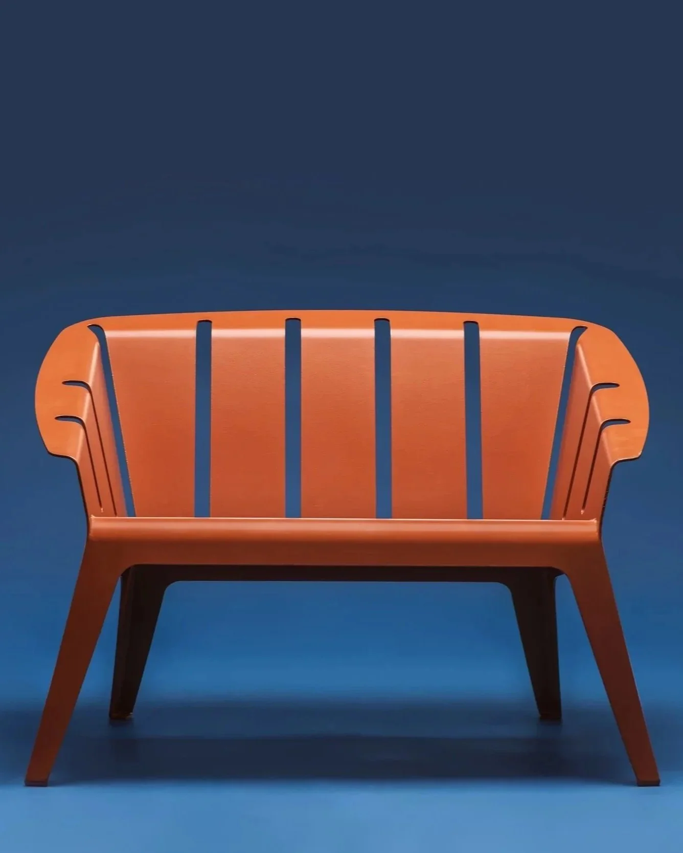 Ein orangefarbenes modernes Gartenmöbelstück vor blauem Hintergrund.