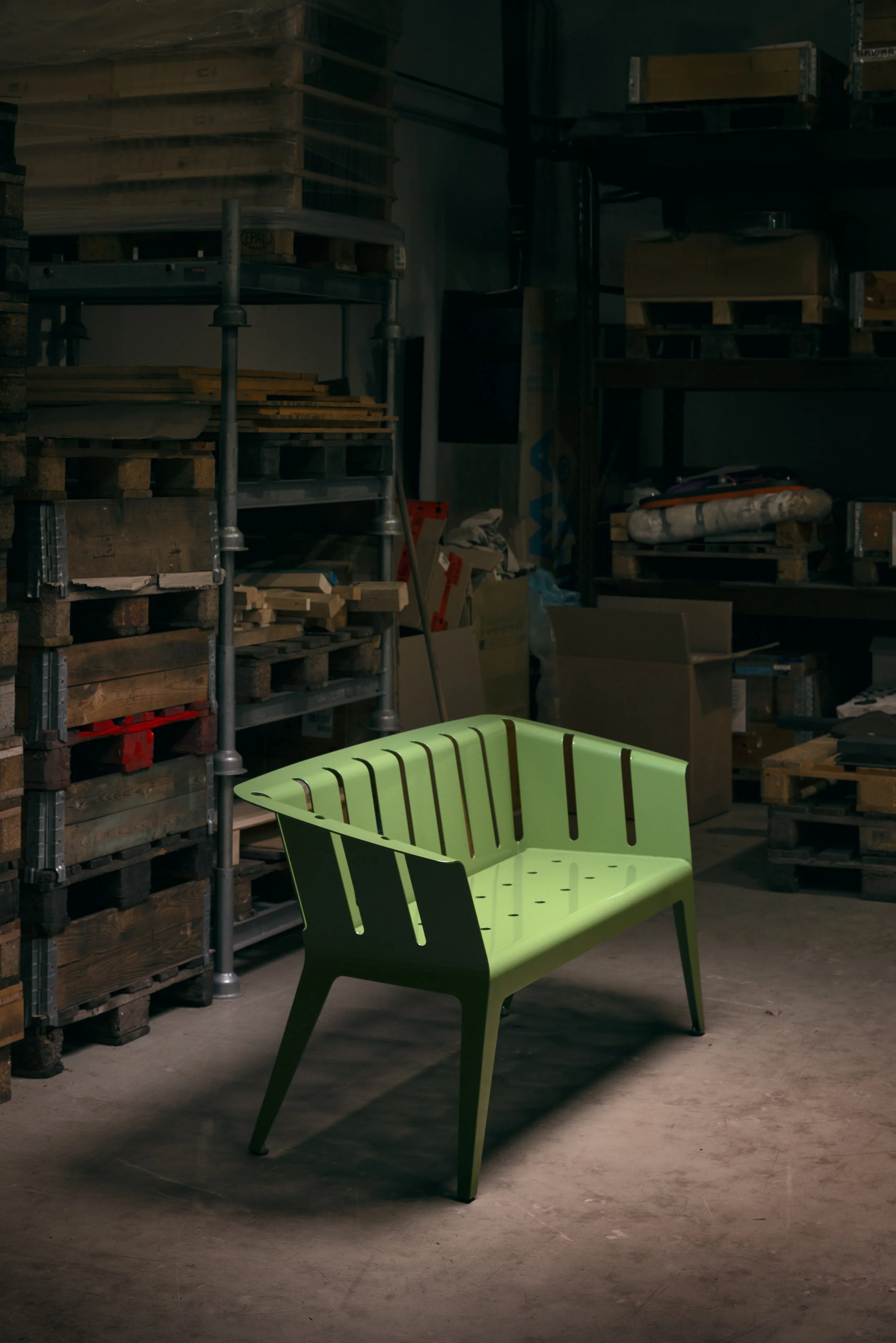 Ein grünes moderne Sitzbank in einem Lagerraum mit Holzregalen und Kartons.