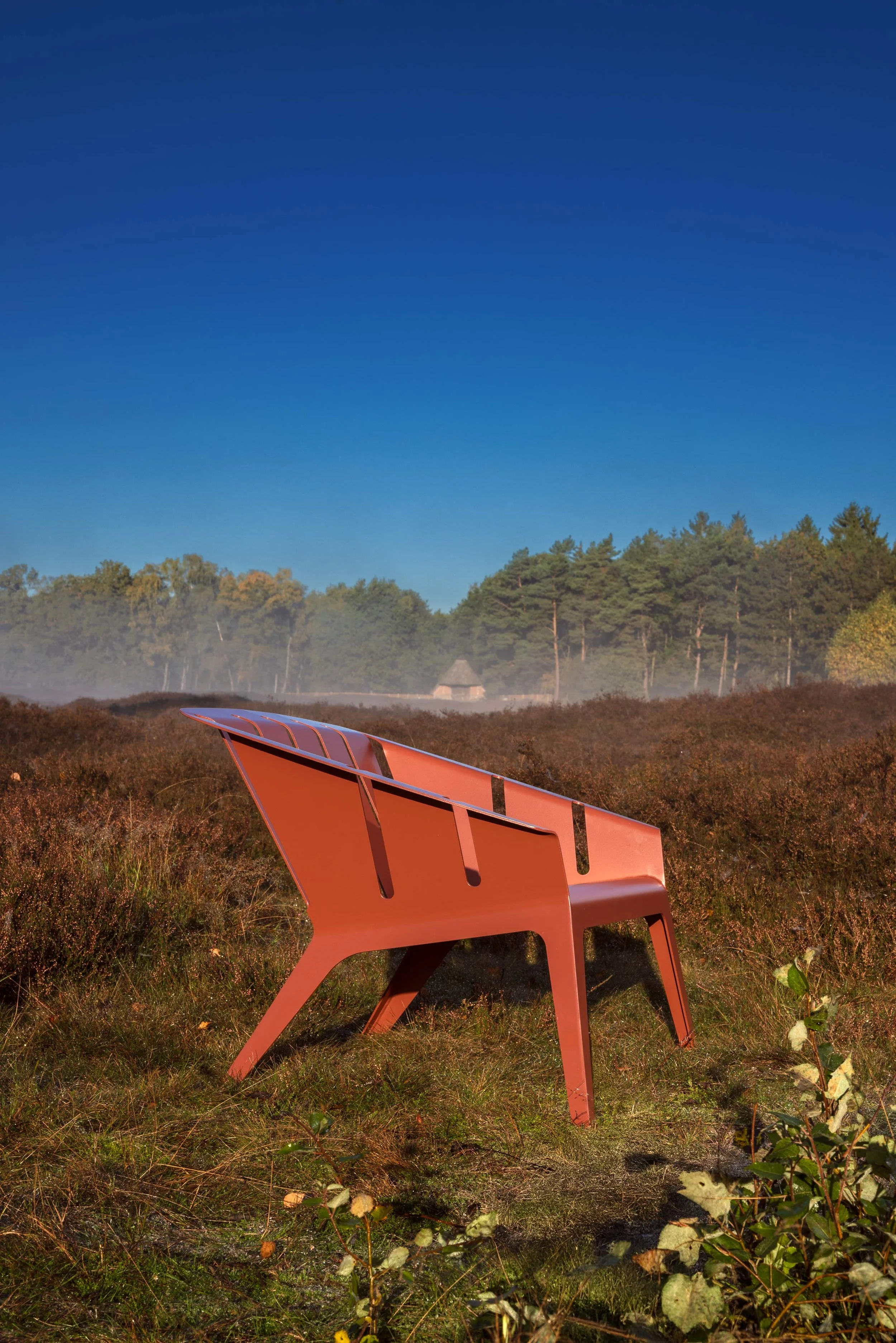 Ein roter, moderne Sitzbank im Freien in einem Heidegebiet mit mehrfarbigem Himmel im Hintergrund.