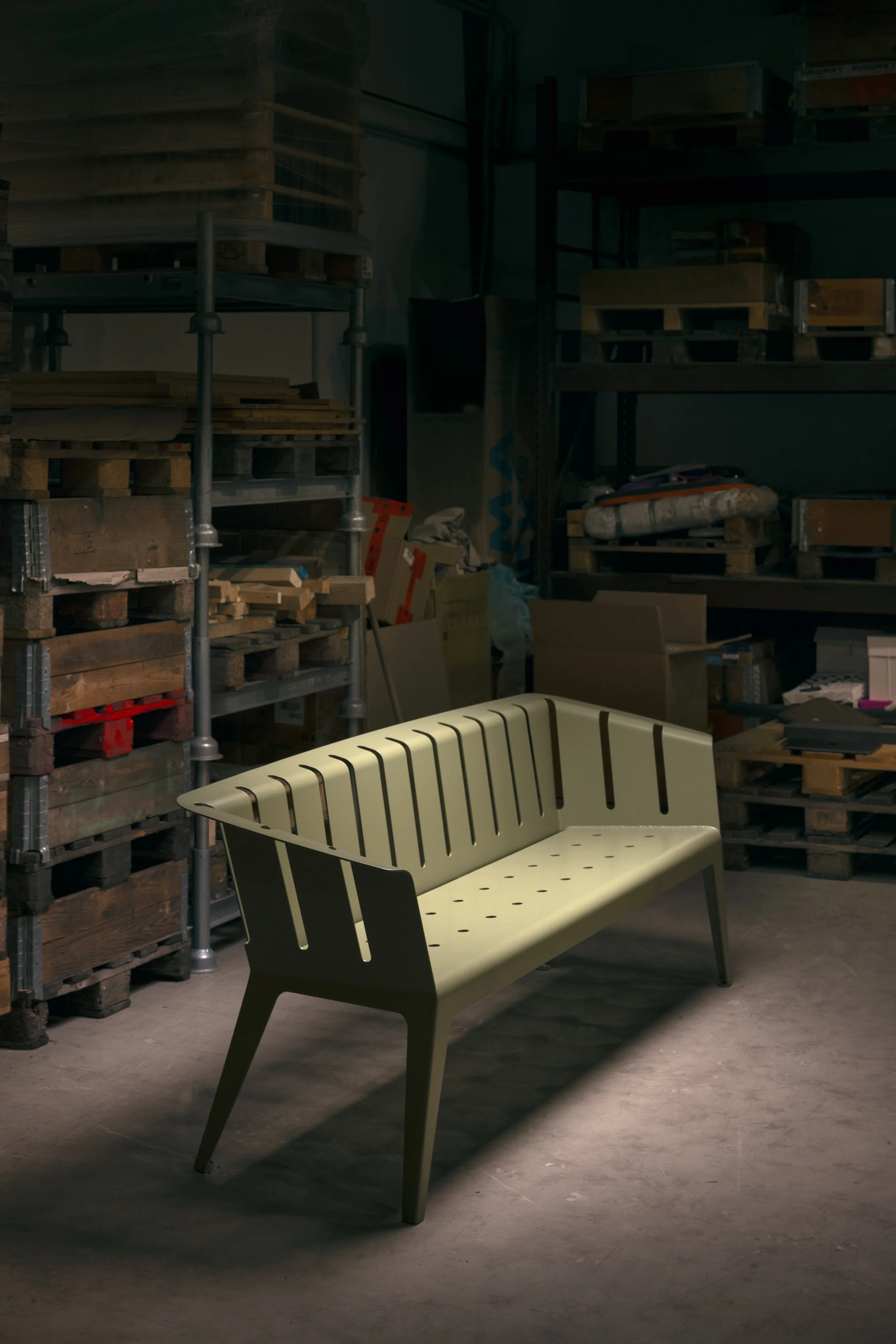 Ein moderner, hellgrüner Gartensitzbank in einem Lagerraum aus Holz und Metall, im Hintergrund Regale mit Holzplatten und Baumaterialien.