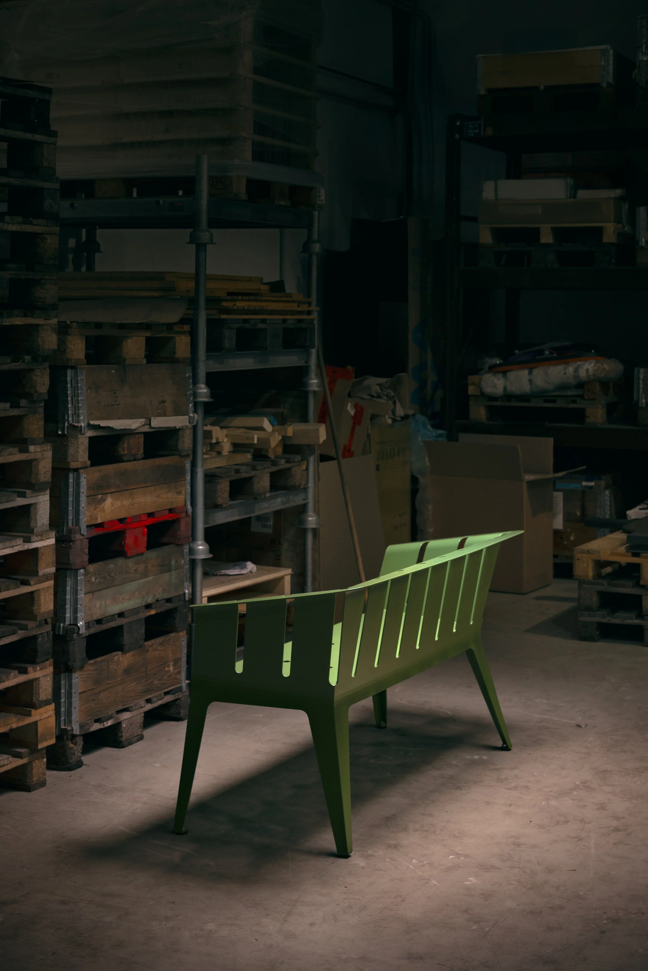 Grüner moderner Holzbϱätsel-Stuhl in einer Lagerhalle mit Holzpaletten und Regalen im Hintergrund.