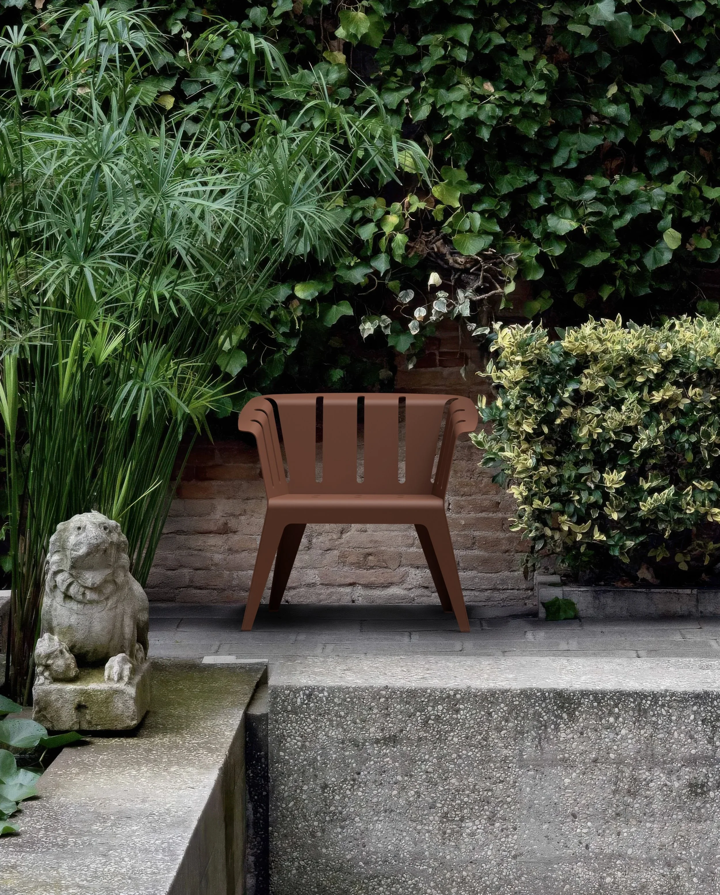 Ein brauner Gartenstuhl auf einer kleinen Terrasse vor einer Mauer mit grünem Bewuchs.